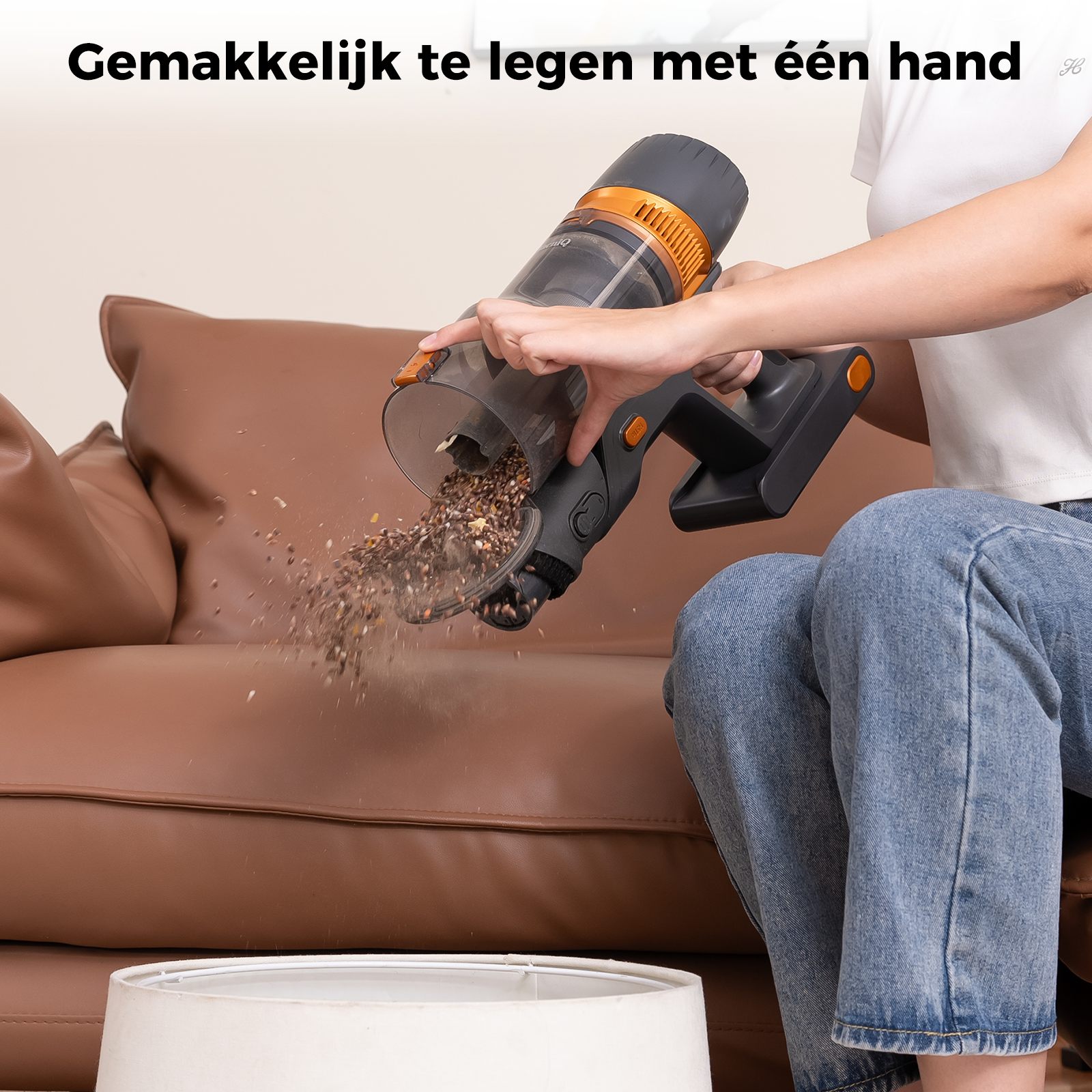 A person emptying a vacuum cleaner. The vacuum is black and orange. Debris is falling into a white container.