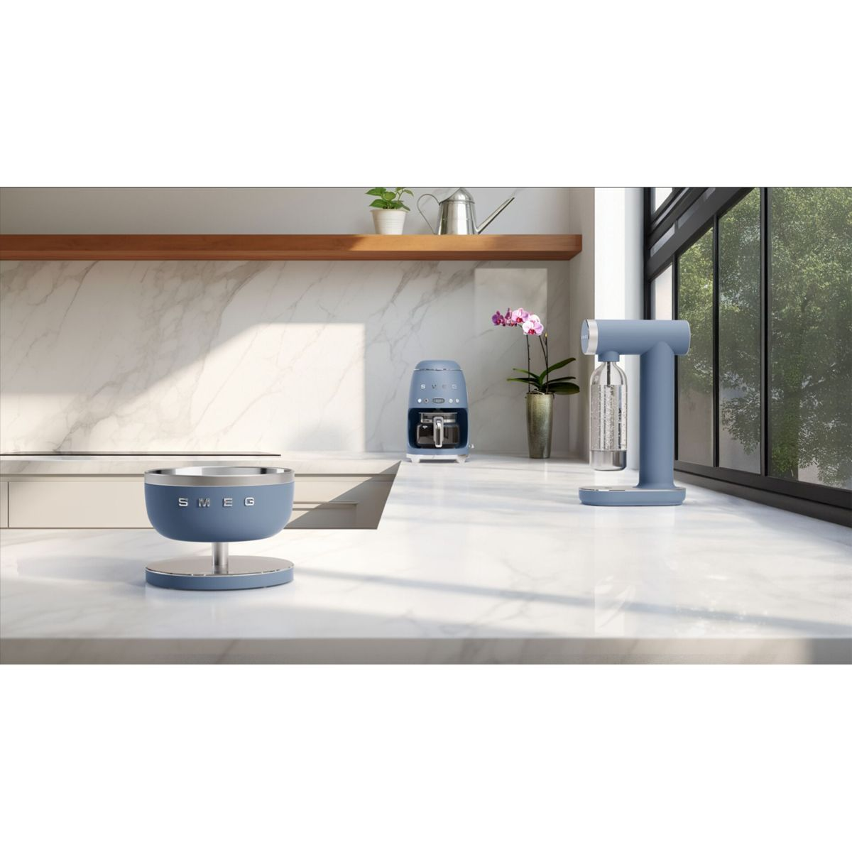 Una encimera de cocina con electrodomésticos SMEG azules: un cuenco, una cafetera y una máquina de soda. Una ventana muestra árboles.