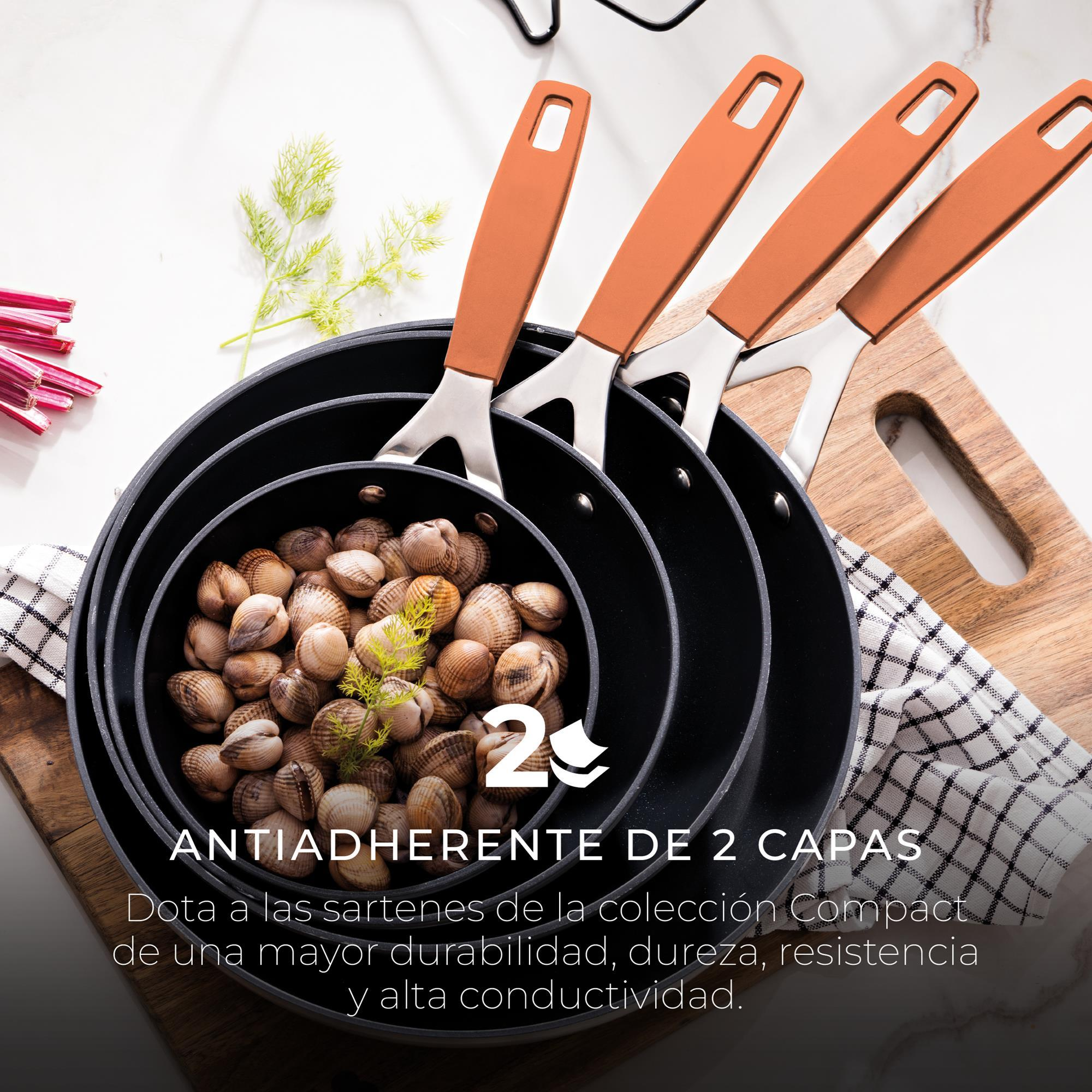 Quattro padelle nere, una piena di vongole, con manici arancioni, su una superficie bianca, con un tagliere e un tovagliolo.