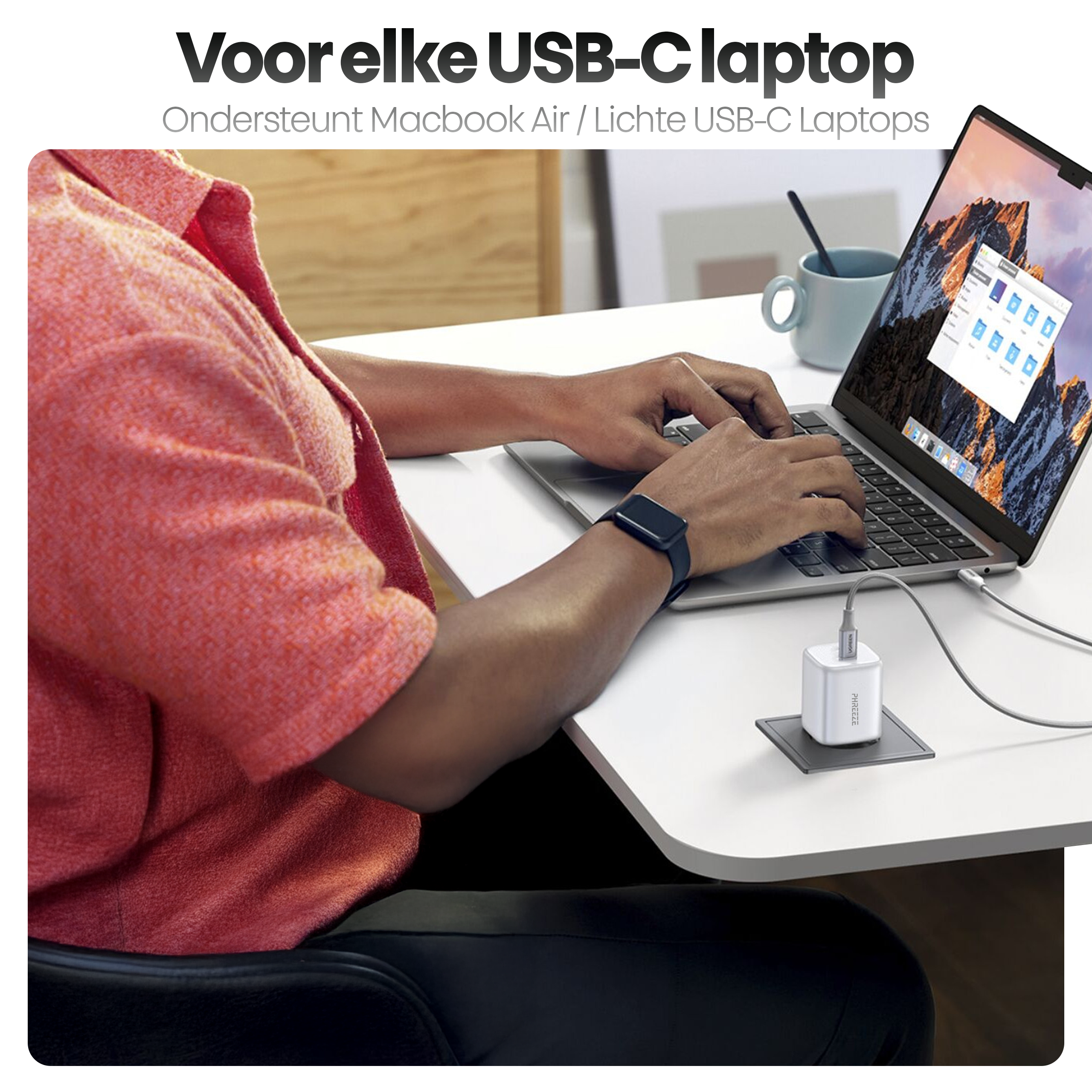 Persoon typt op laptop, verbonden met een oplader. Tekst bovenaan, een beker en een zwart horloge zijn ook zichtbaar.