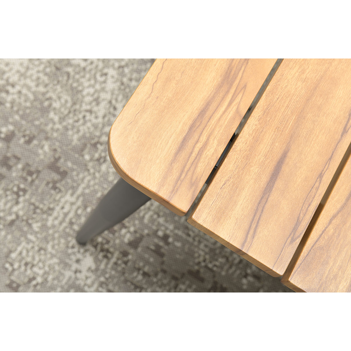 Gros plan sur un coin de table en bois avec un pied gris. La table est brun clair avec le grain du bois visible, posée sur un tapis à motifs.