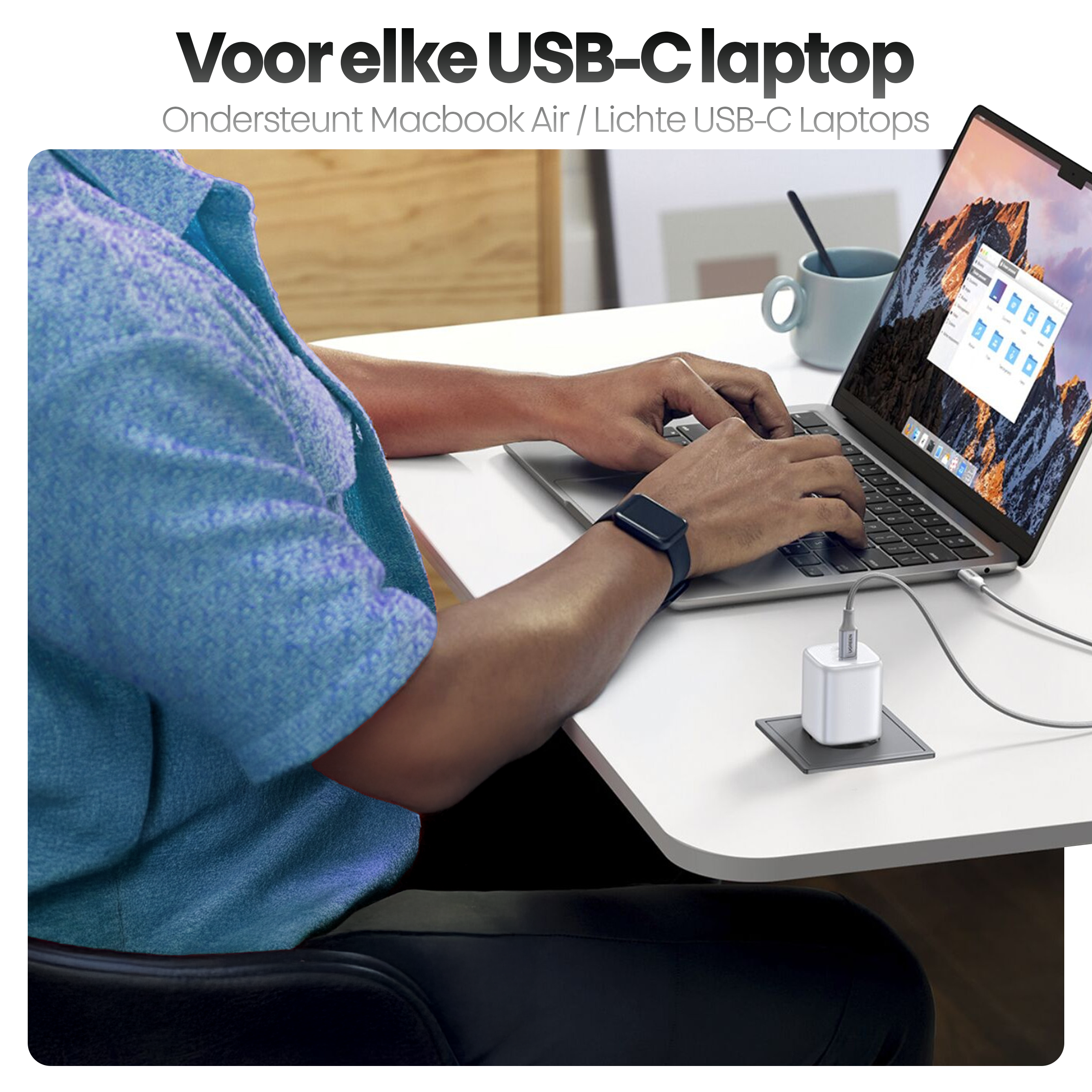 Een persoon typt op een laptop met een oplader aangesloten. Een kopje en tekst staan op de achtergrond.