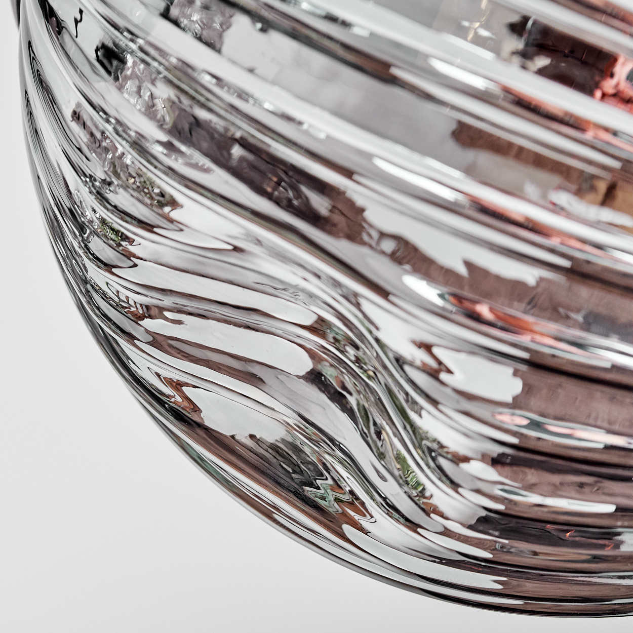 Nahaufnahme eines transparenten Glasobjekts mit wellenförmiger, geriffelter Textur. Reflexionen von Braun und Rosa sind sichtbar.