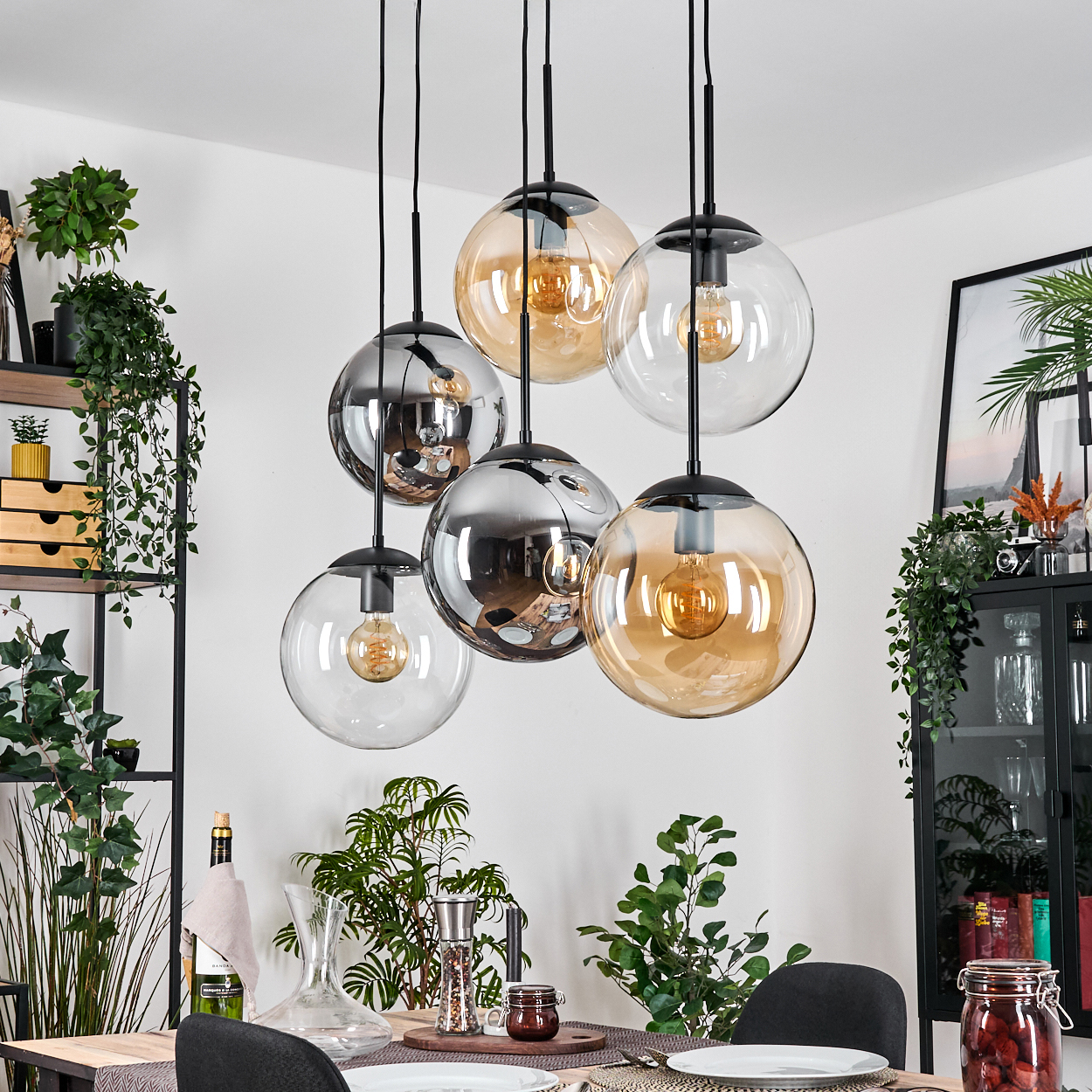 Esszimmer mit hängenden Kugelleuchten. Klare und bernsteinfarbene Glaskugeln, Pflanzen, ein Esstisch und verschiedene Dekorationen.