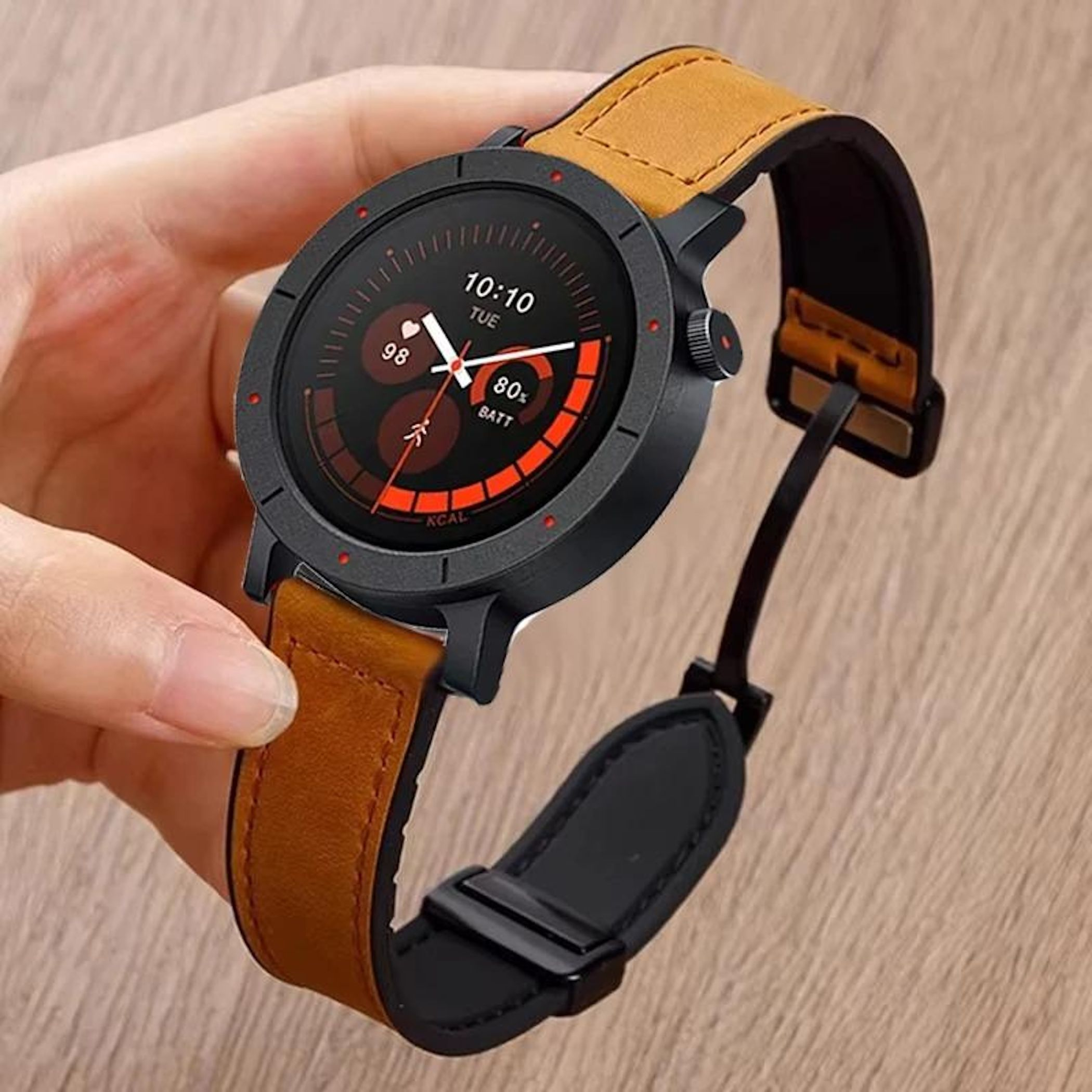 Eine Hand, die eine schwarze Smartwatch mit braunem Lederarmband hält. Der Bildschirm zeigt Zeit und Akku.