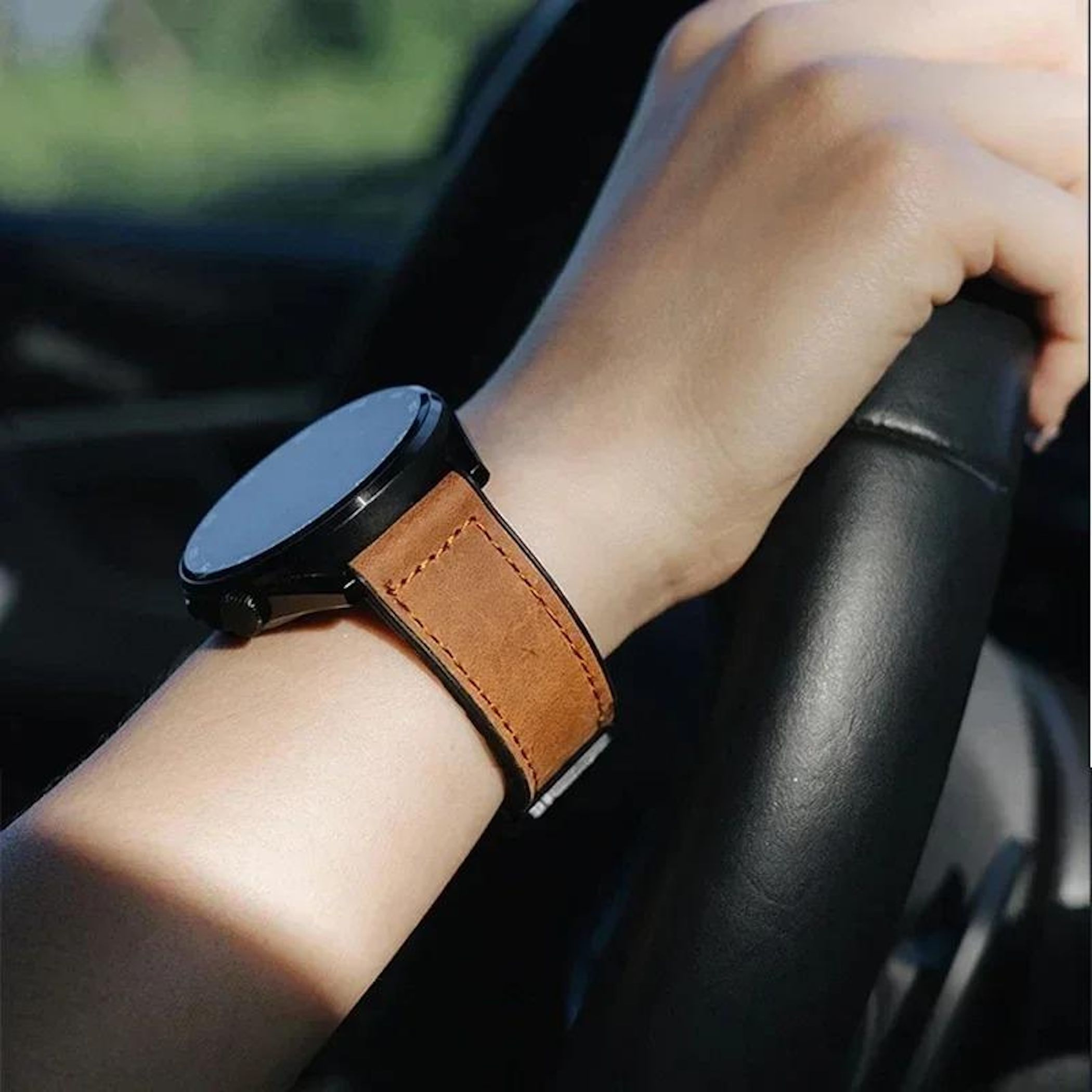 Arm mit Uhr am Handgelenk, hält Lenkrad. Die Uhr hat ein braunes Lederarmband.