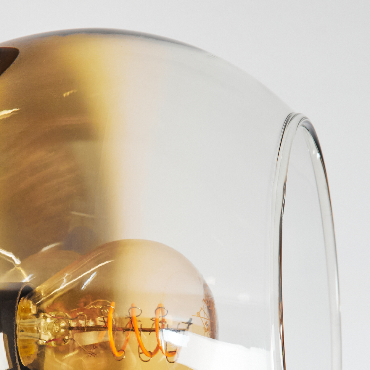 Nahaufnahme einer Leuchte mit Glasabdeckung. Eine bernsteinfarbene Glühbirne ist in der Glaskuppel vor weißem Hintergrund sichtbar.