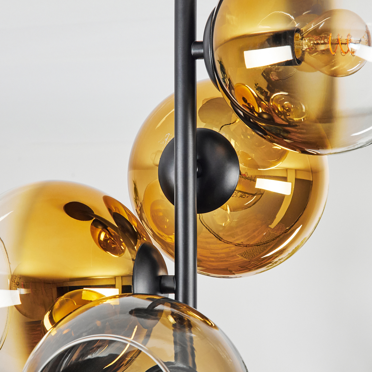 Eine moderne Lampe mit mehreren bernsteinfarbenen Glaskugeln, schwarzem Metallrahmen und sichtbaren Glühbirnen auf weißem Hintergrund.