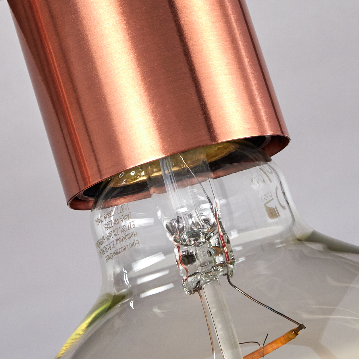 Nahaufnahme einer Glühbirne. Kupferfarbener Lampenschirm und eine klare Glasbirne mit sichtbaren Filamenten und gedrucktem Text.