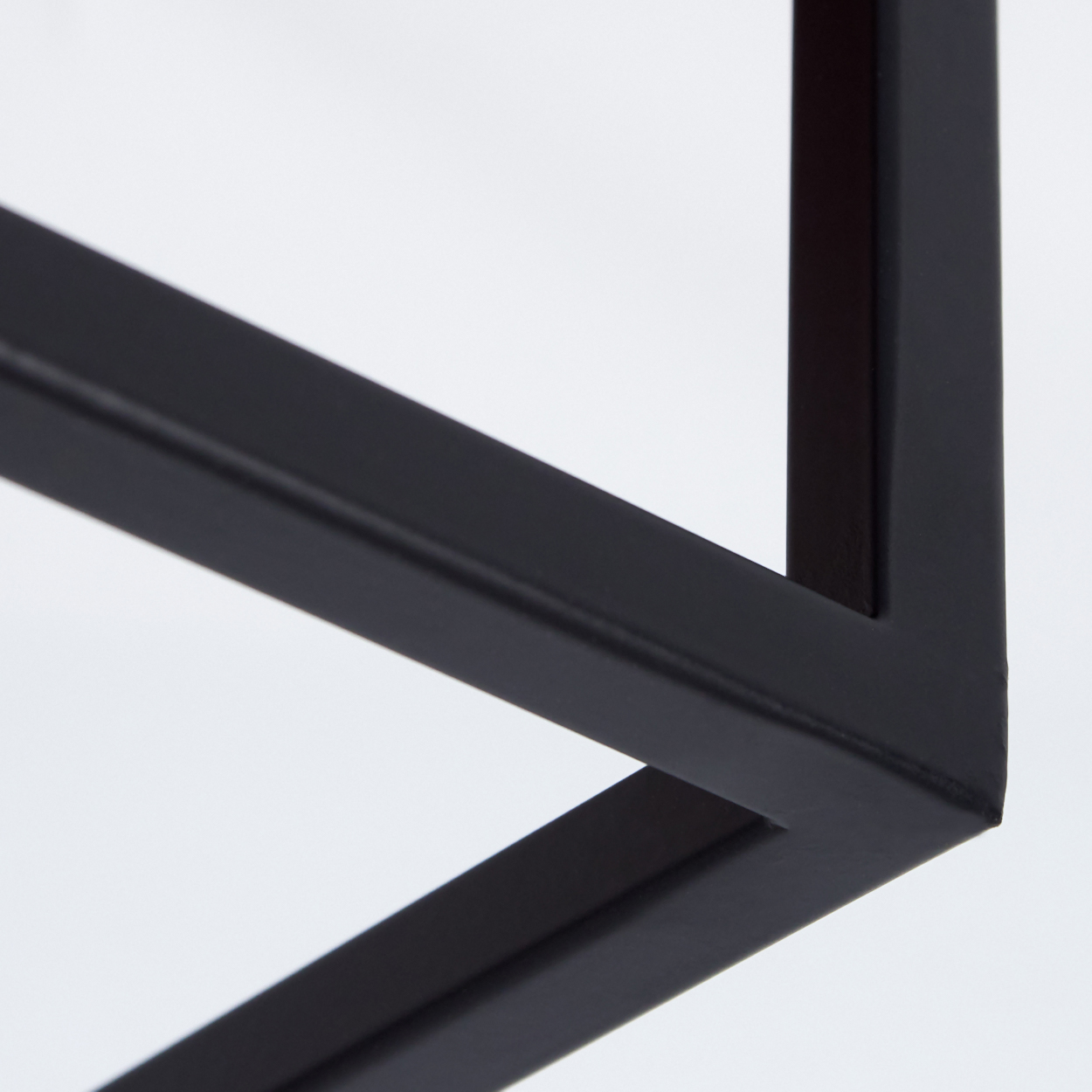 Nahaufnahme eines schwarzen Metallrahmens vor weißem Hintergrund. Der Rahmen bildet geometrische Formen.