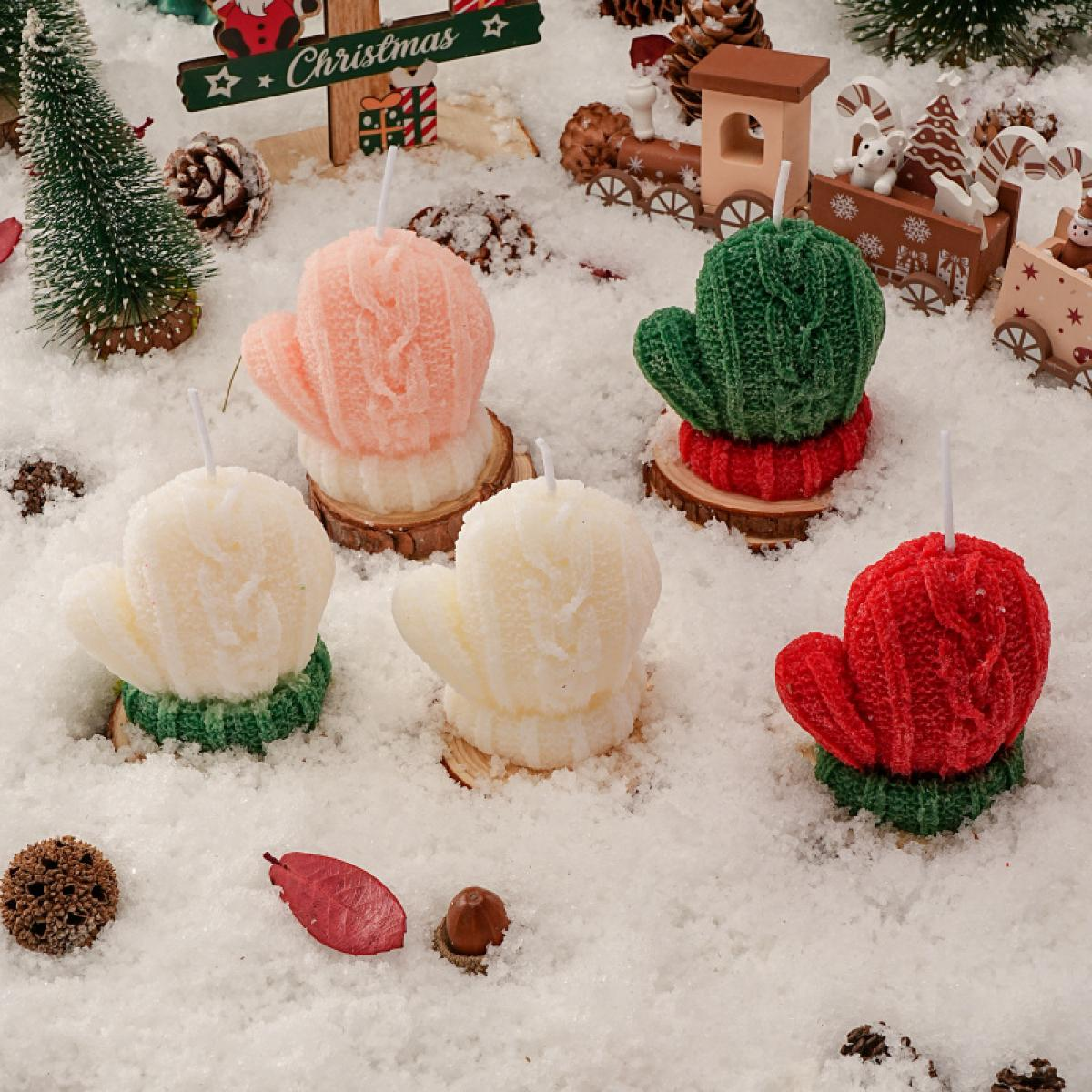 Weihnachtsszene mit handschuhförmigen Kerzen in Rosa, Grün, Weiß und Rot auf einer schneebedeckten Oberfläche. Dekorationen und ein Schild.