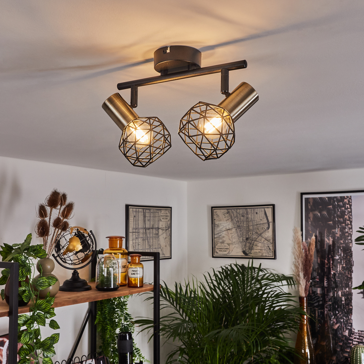 Zwei geometrische Lampen an der Decke, die einen Raum mit Pflanzen und einem Regal beleuchten. Karten und Dekoration sind sichtbar.