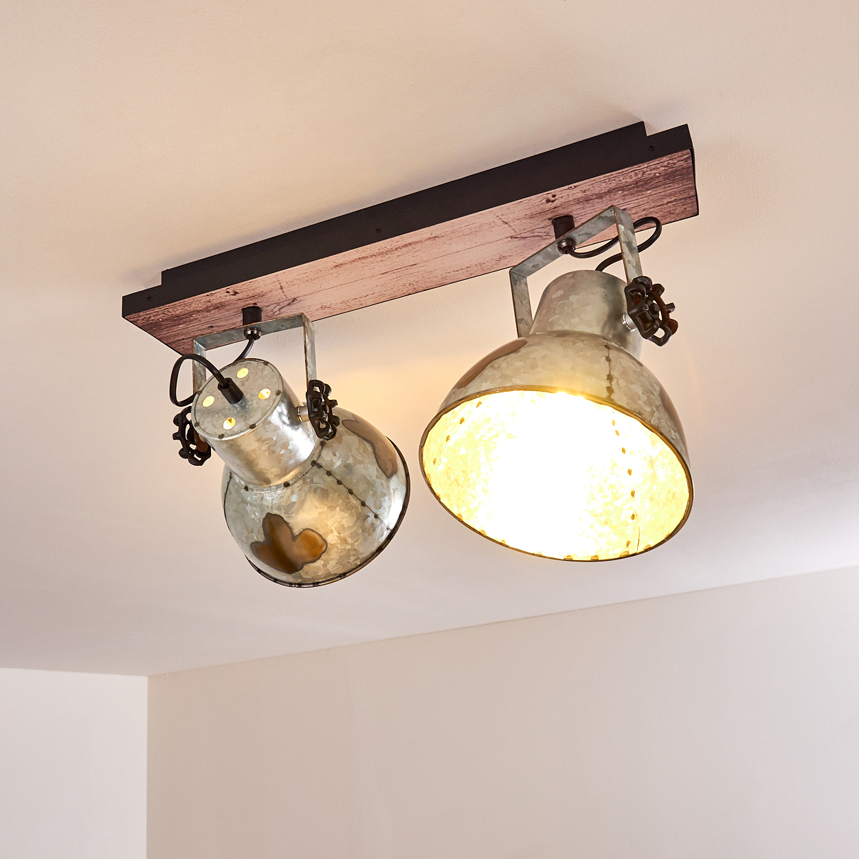 Zwei Metallstrahler mit sichtbaren Glühbirnen hängen an einem Holzbalken, der an einer weißen Decke befestigt ist. Das Licht ist an.