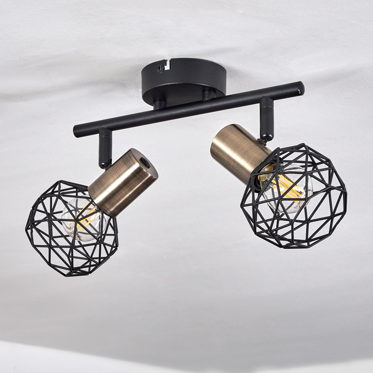 Moderne Deckenleuchte mit zwei bronzefarbenen Strahlern in schwarzen geometrischen Käfigen, montiert auf einem schwarzen Rahmen auf Weiß.