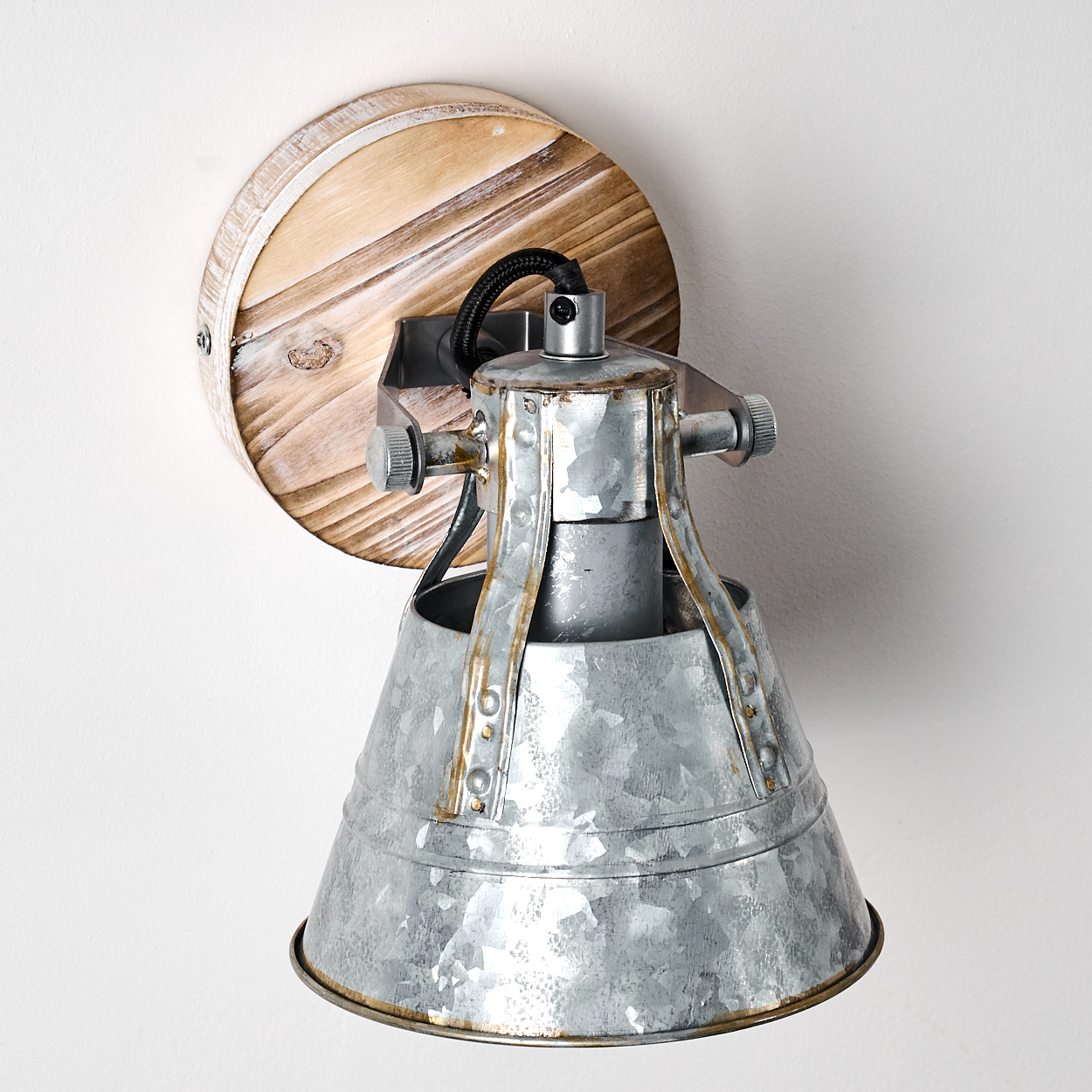 Eine Metall-Wandleuchte mit Holzsockel. Die Lampe hat einen konischen Schirm und eine silberne Oberfläche, an einer weißen Wand montiert.