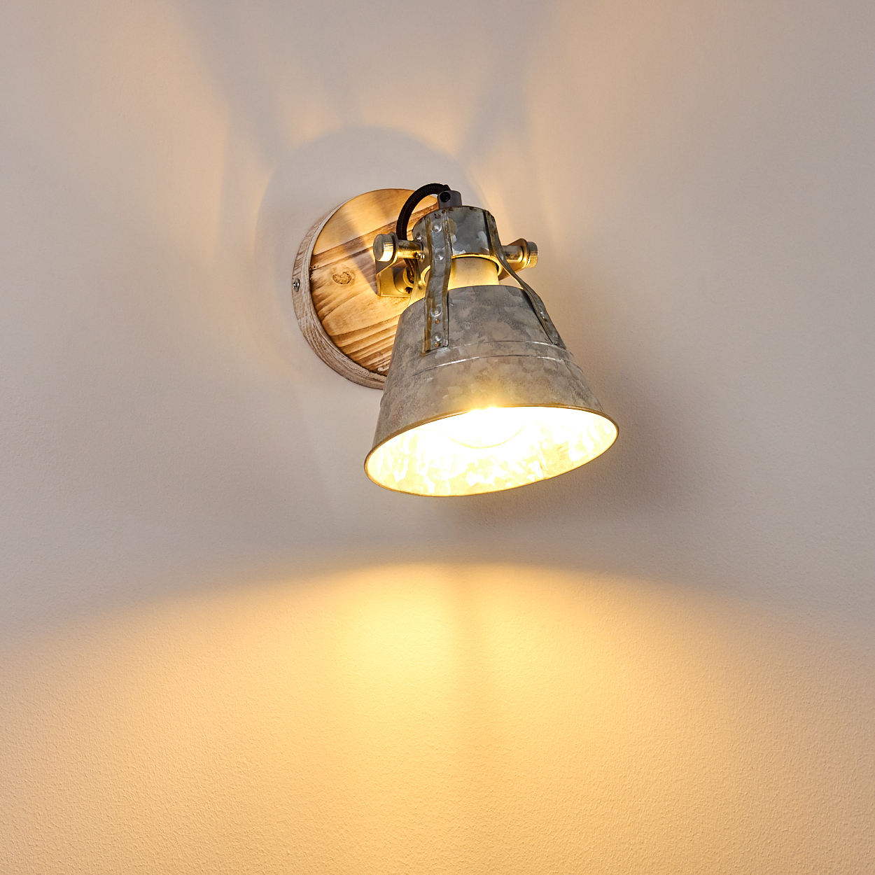 Eine Metall-Wandleuchte mit Holzsockel ist an einer weißen Wand montiert und wirft ein warmes Licht.
