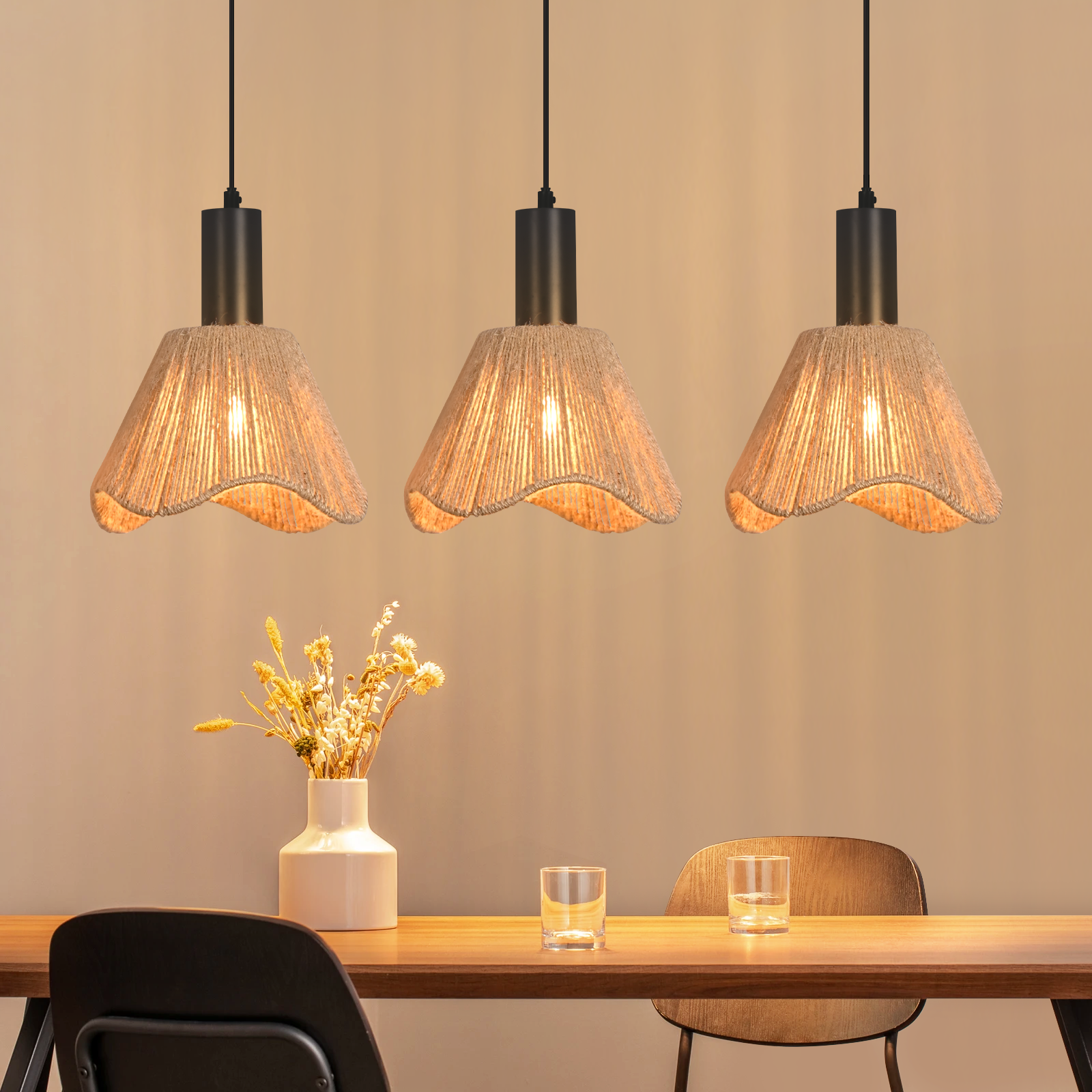 Drei Pendelleuchten mit gewebten Schirmen hängen über einem Tisch mit einer Blumenvase, zwei Gläsern und einem Stuhl.