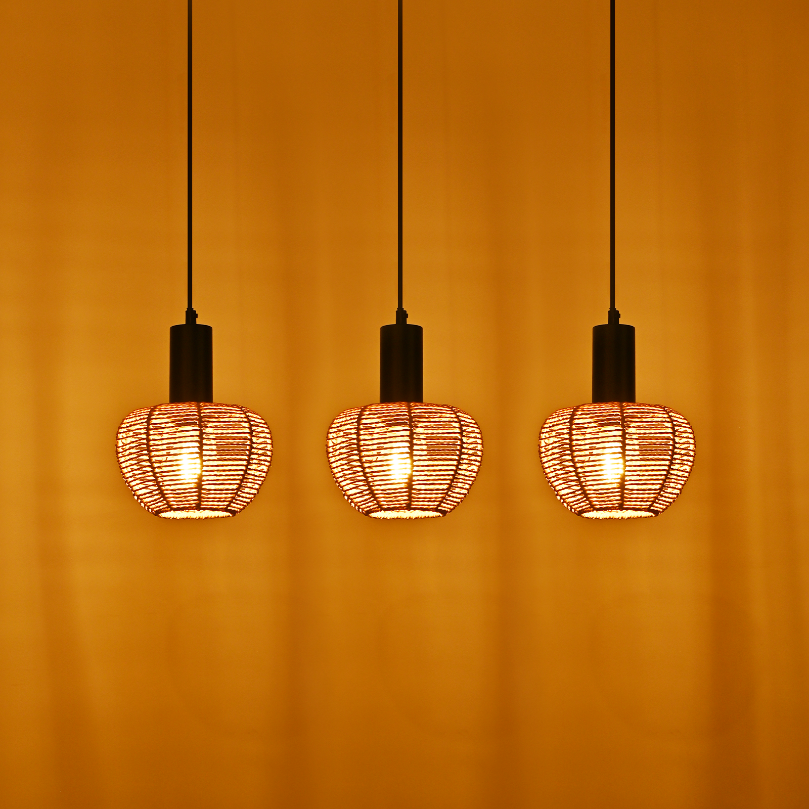 Drei Hängeleuchten mit gewebten Schirmen hängen vor einer orangefarbenen Wand. Die Leuchten haben schwarze Stiele und geben warmes Licht ab.
