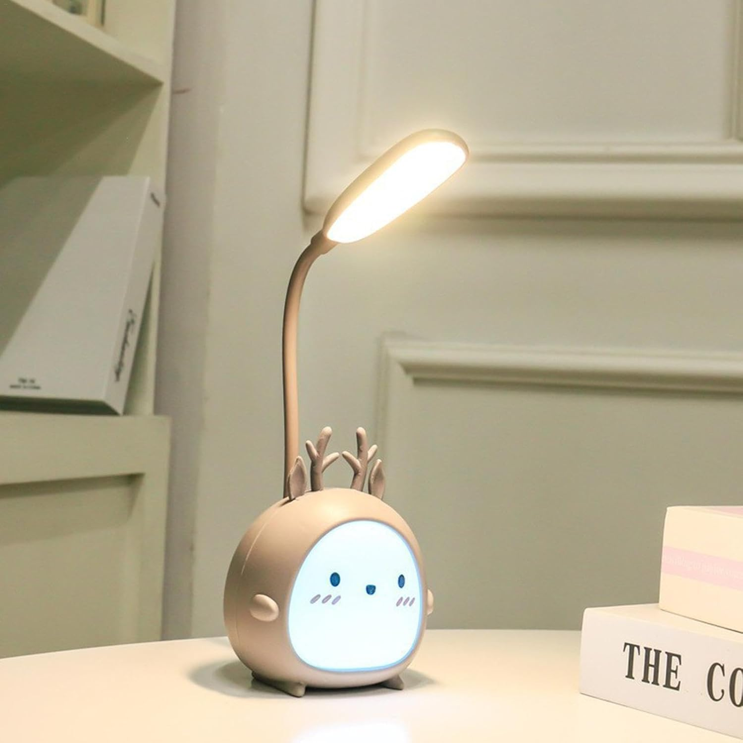 Eine beige Cartoon-Hirschlampe mit hellem Licht auf einem weißen Tisch. Bücher sind rechts und ein Regal im Hintergrund.