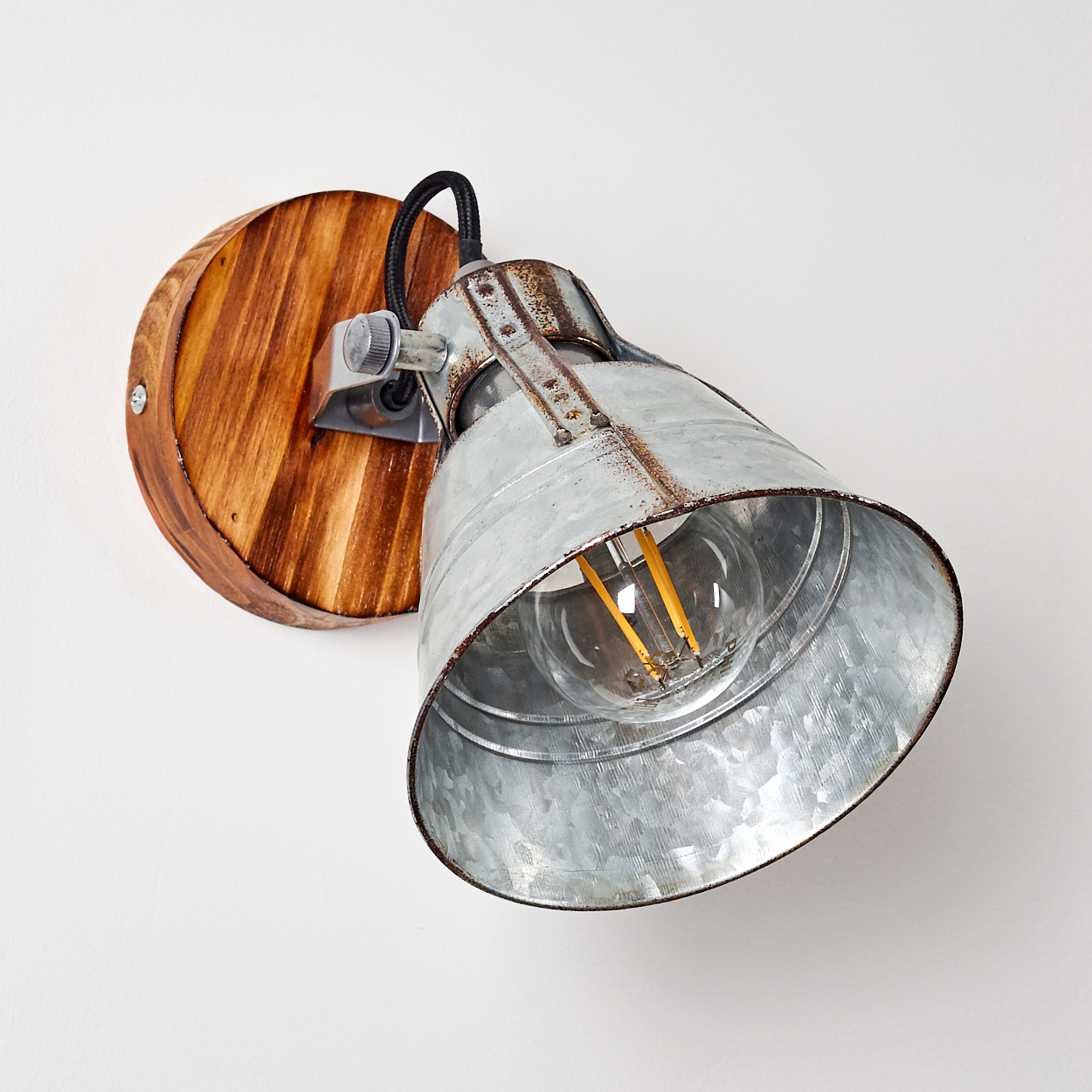 Eine rustikale Wandlampe mit Holzsockel und Metallschirm, einschließlich Glühbirne. Die Lampe ist an einer weißen Wand montiert.