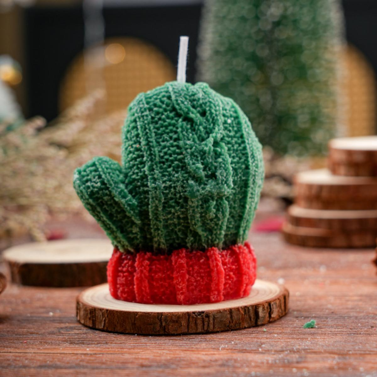 Eine grüne, kaktusförmige Kerze mit roter Basis steht auf einem Holzuntersetzer. Im Hintergrund befinden sich Holzscheiben und Weihnachtsdeko.