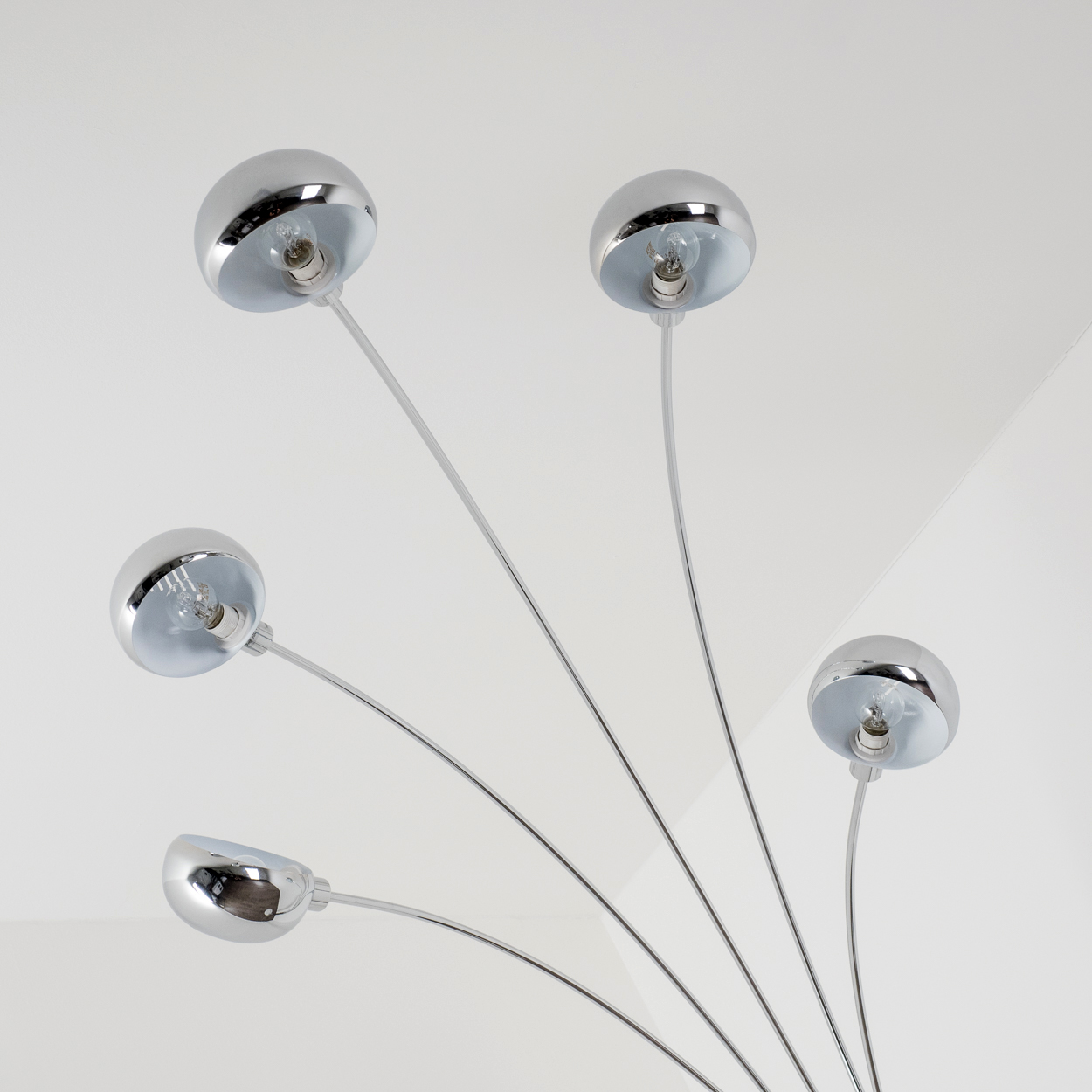 Eine moderne Chrom-Kronleuchter mit fünf kugelförmigen Leuchten. Jede Leuchte hat eine Glühbirne. Der Hintergrund ist weiß.