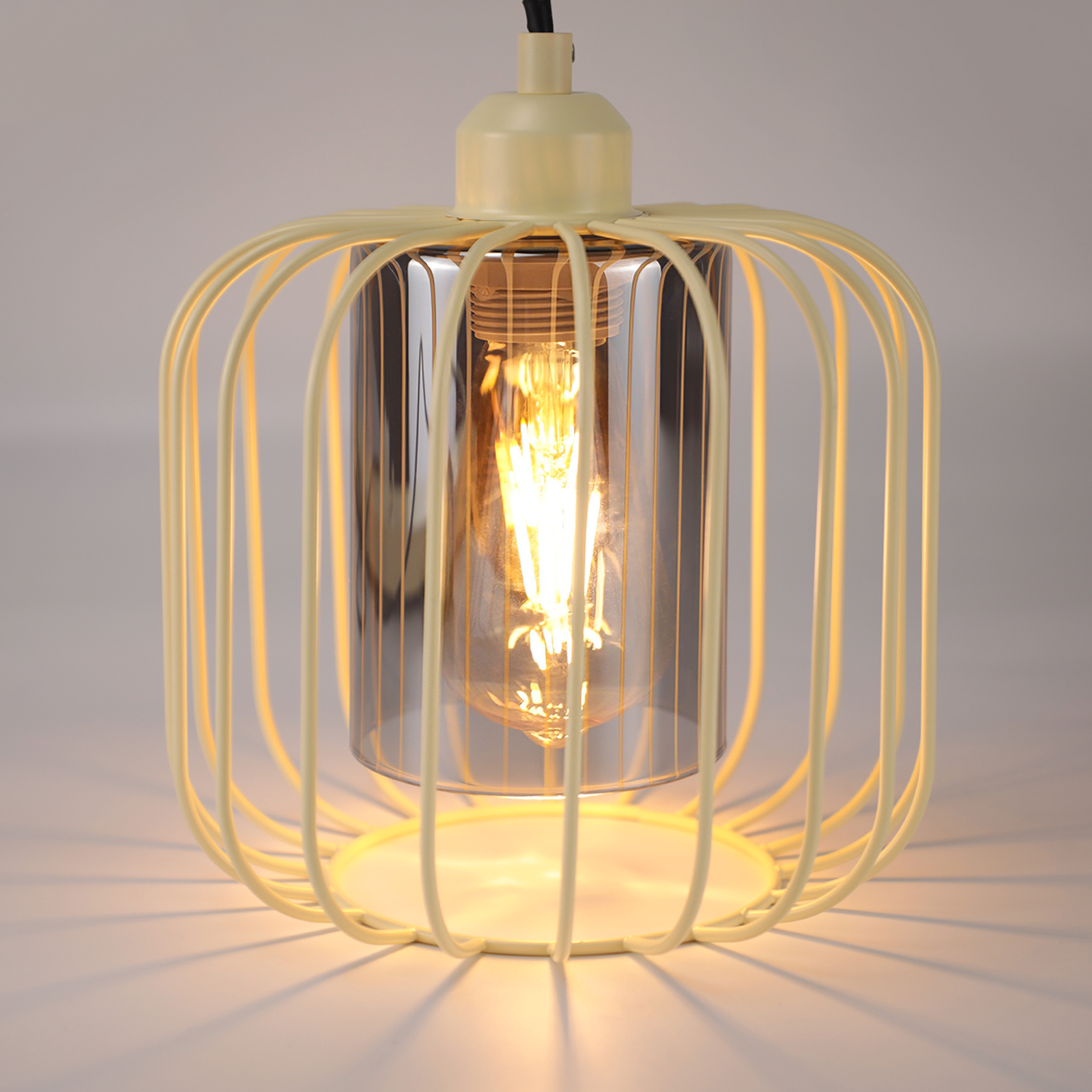Eine cremefarbene Pendelleuchte aus Metallkäfig mit einer beleuchteten Edison-Glühbirne im Inneren.
