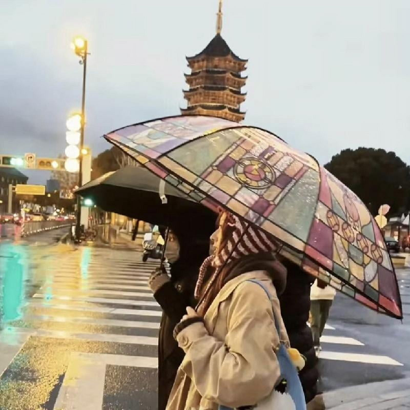 Menschen mit Regenschirmen überqueren eine Straße. Ein bunter Regenschirm ist vor einer Pagode. Es regnet.