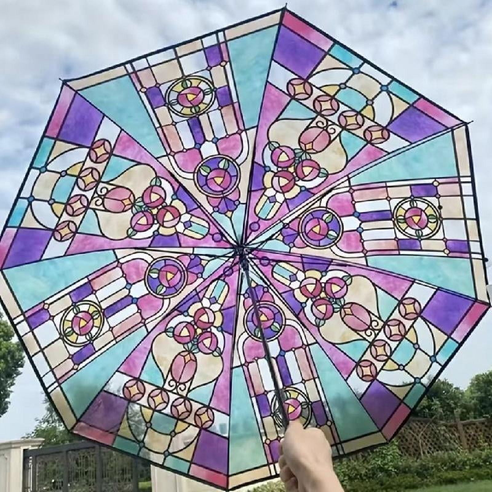 Ein bunter Regenschirm mit Buntglasdesign, vor einem bewölkten Himmel gehalten. Das Design umfasst florale und geometrische Muster.