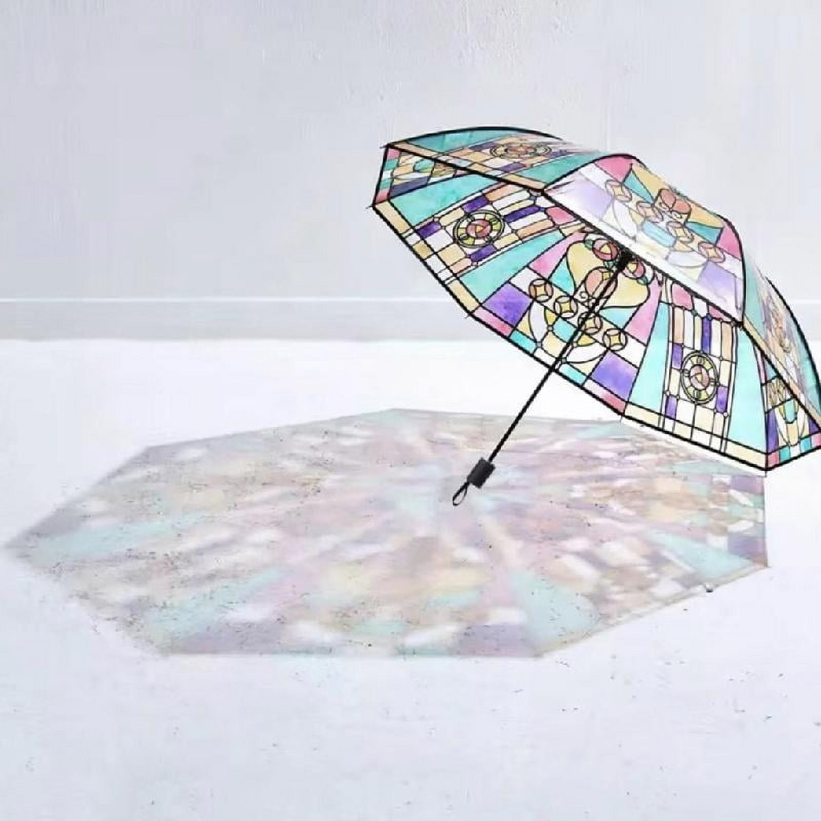 Ein bunter Regenschirm mit Buntglasdesign ist geöffnet und wirft einen Schatten auf eine weiße Oberfläche. Der Hintergrund ist weiß.