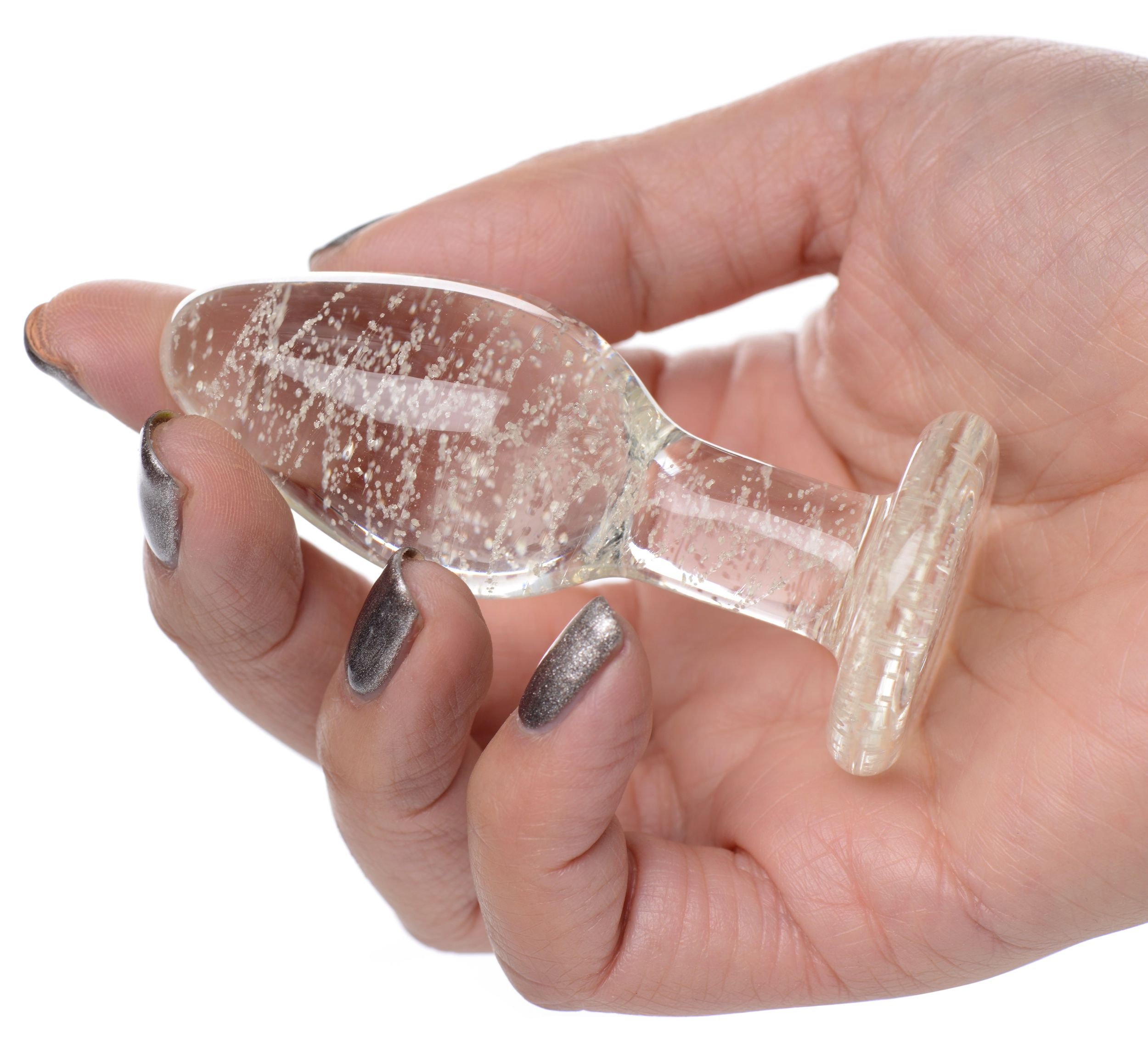 Eine Hand hält ein klares Sexspielzeug aus Glas. Die Hand hat silbernen Nagellack. Der Hintergrund ist weiß.