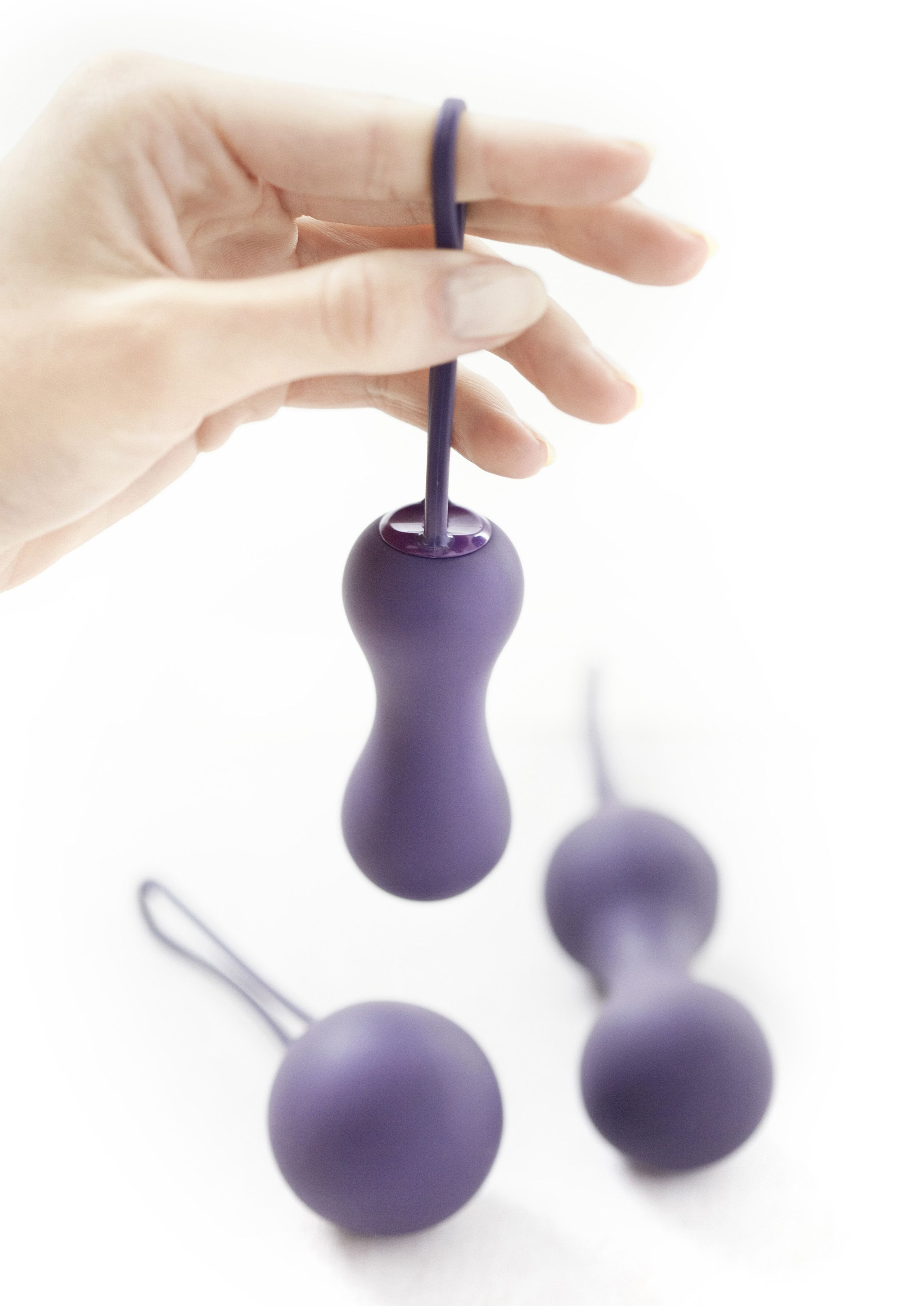 Mano sosteniendo un juguete sexual morado. Dos juguetes más están sobre fondo blanco.