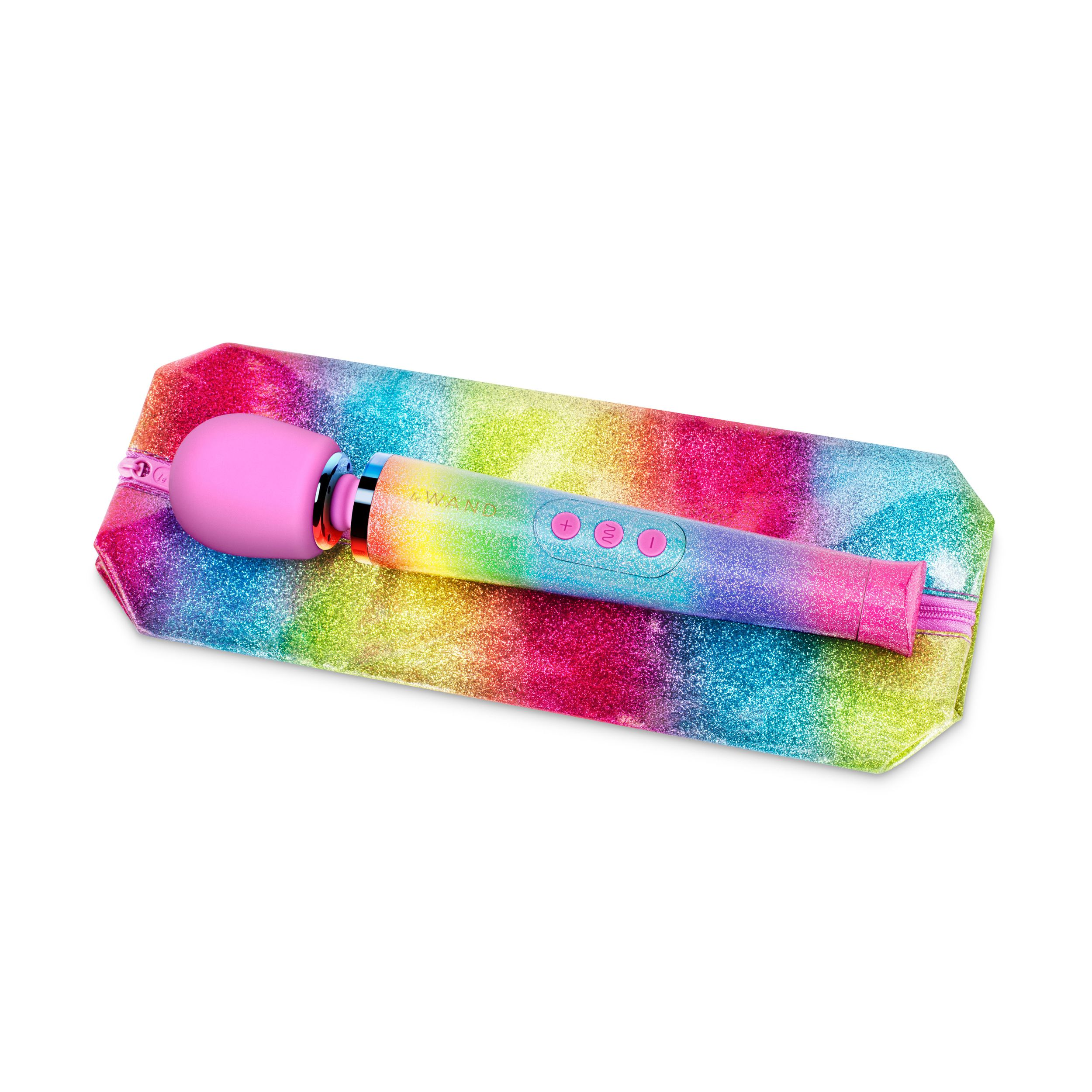 Ein pinkfarbener Vibrator mit Regenbogenakzenten liegt auf einer glitzernden Regenbogenhülle vor weißem Hintergrund.