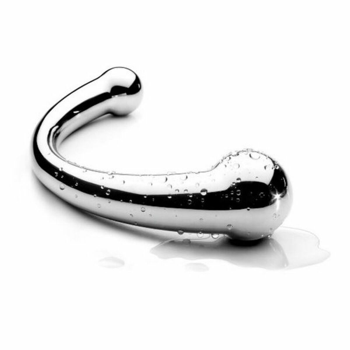 Ein verchromtes Sexspielzeug liegt auf einer weißen Oberfläche mit Wassertropfen. Das Objekt hat eine gebogene Form mit zwei bauchigen Enden.