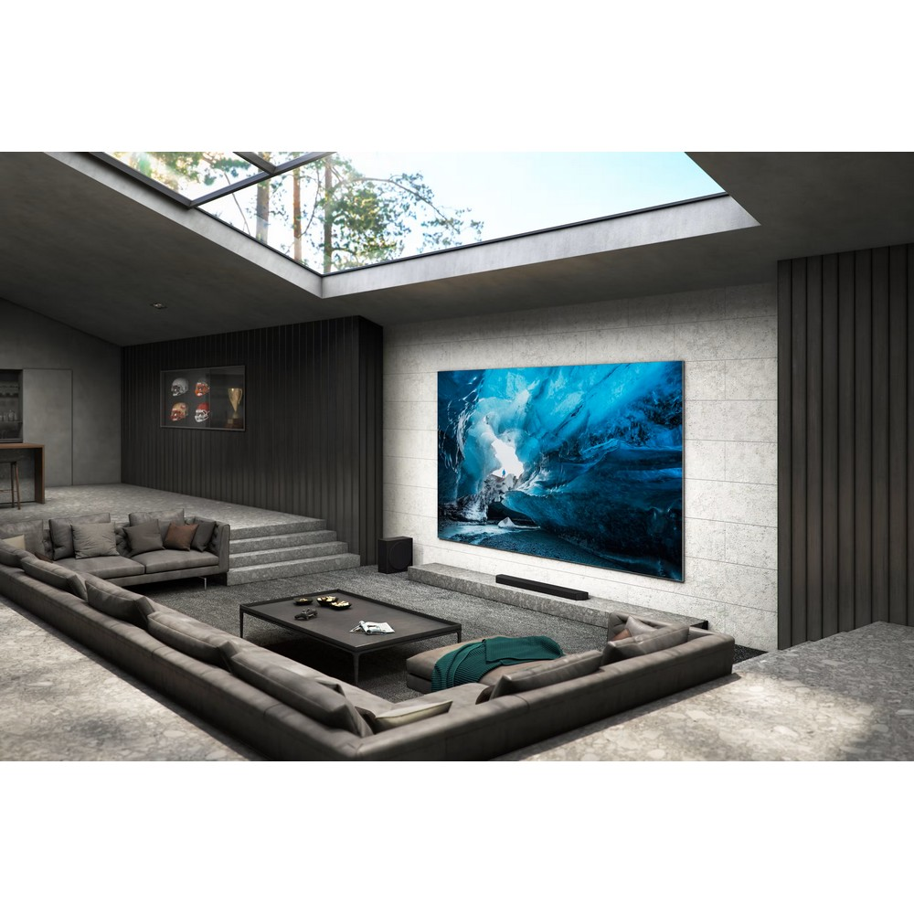 Un moderno soggiorno con una grande TV che mostra un'immagine blu. Sono presenti un divano grigio, un tavolino e un lucernario.