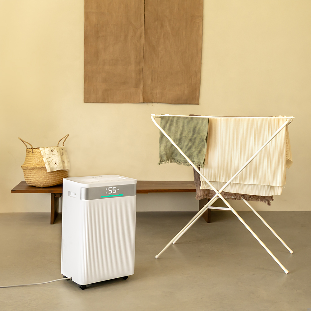 A white dehumidifier, clothes drying rack with towels, a basket with a cloth, and a brown paper on the wall.