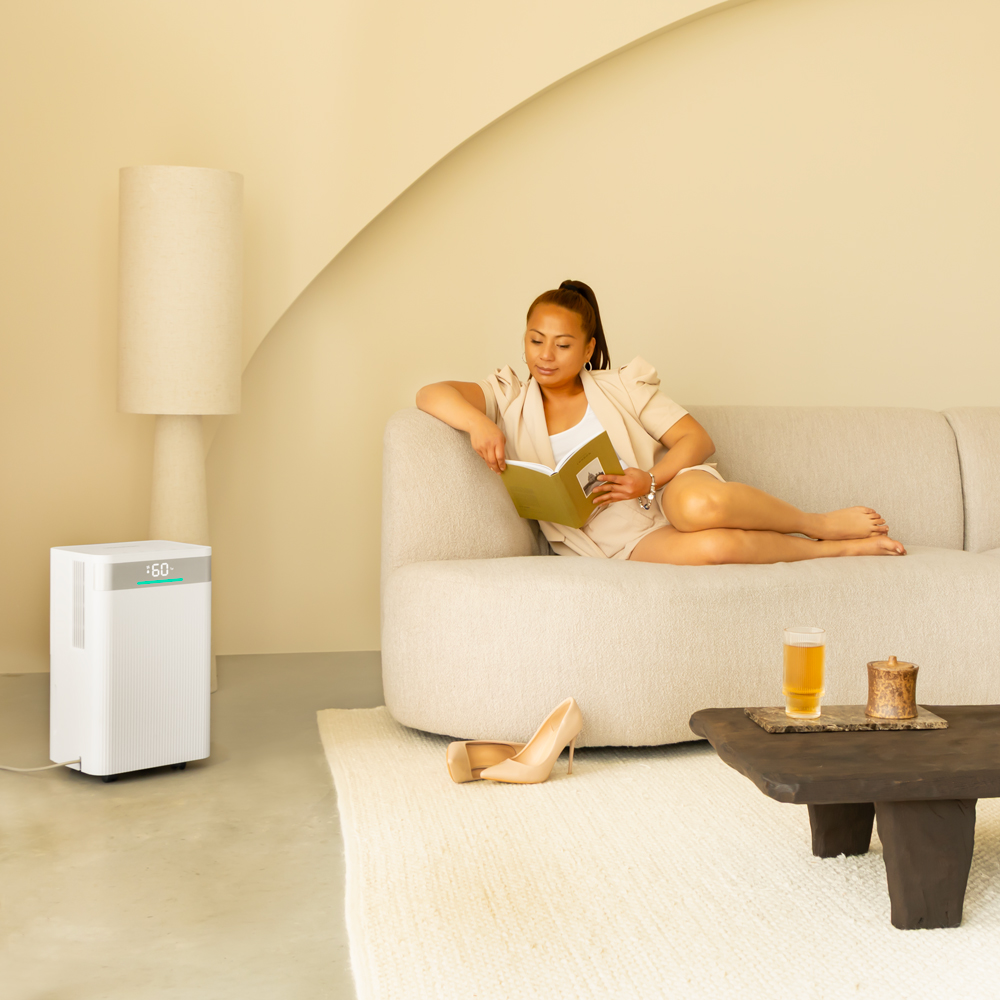 Woman reads on sofa. Shoes, coffee table with drink, lamp, and air purifier are in the room. Beige color scheme.