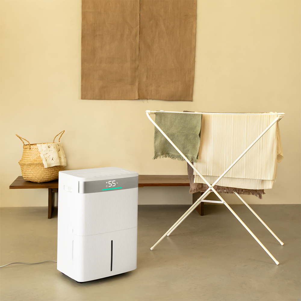 A white dehumidifier, clothes drying rack, and a basket on a bench. Towels and clothes are on the rack. Beige wall and floor.