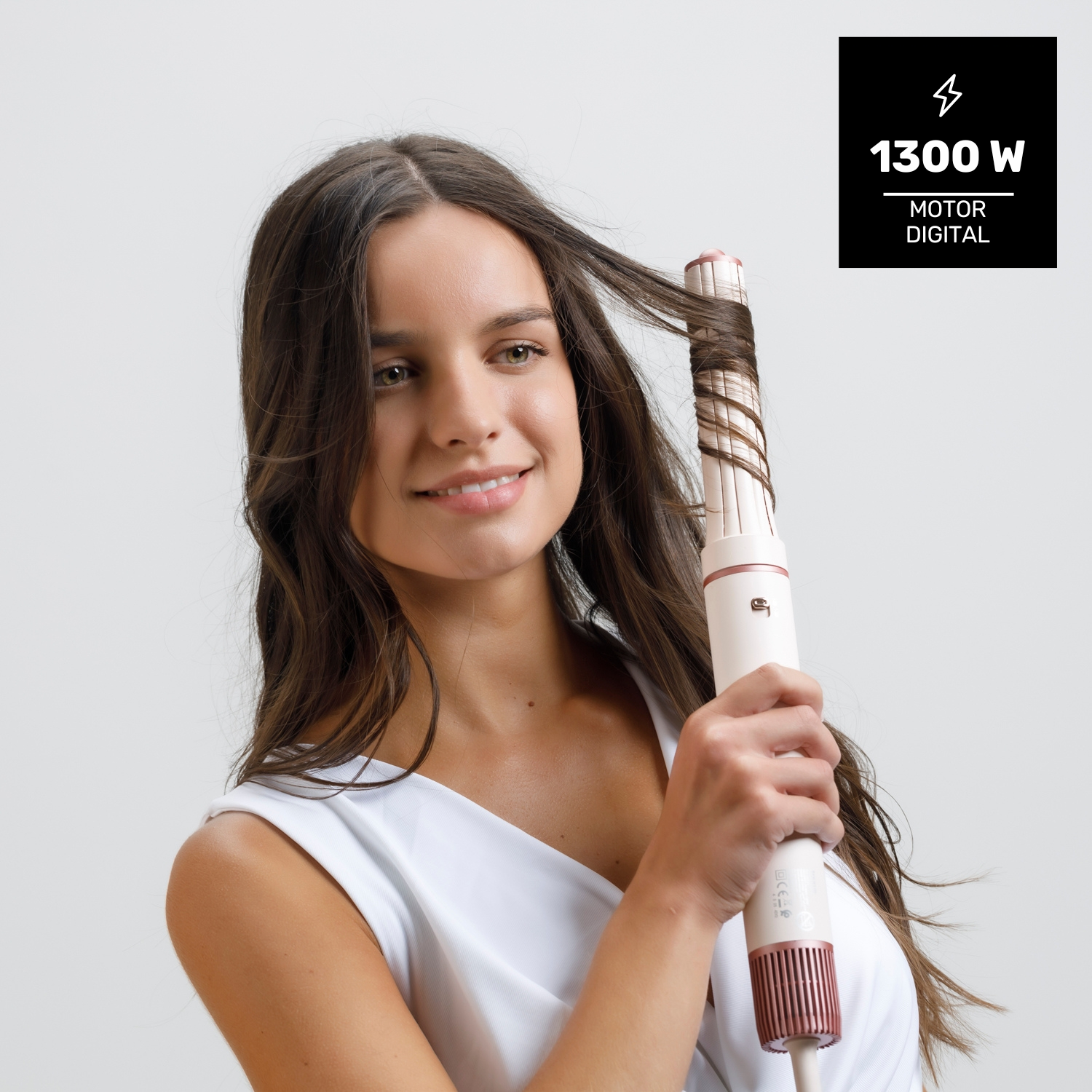 Una donna si arriccia i capelli con un ferro arricciacapelli. Sorride, indossando un top bianco. Una scatola nera mostra 1300W e motore digitale.