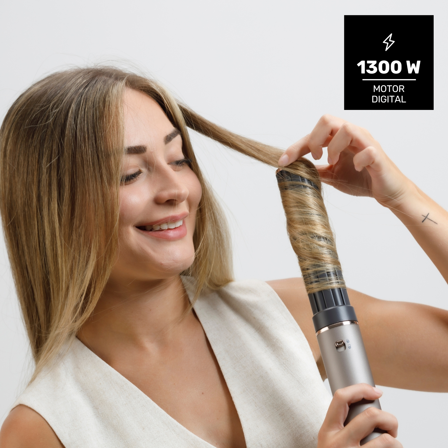 Una mujer se riza el pelo rubio con un rizador plateado. Sonríe, sosteniendo el pelo. Una caja negra en el fondo muestra información de potencia.