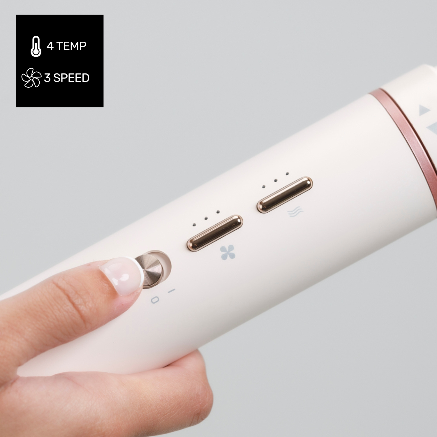 Una mano preme un pulsante su uno strumento per capelli bianco. Ci sono pulsanti per la temperatura e la velocità. Lo sfondo è grigio.