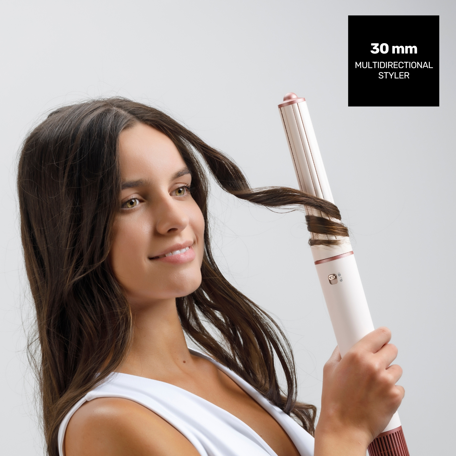 Una donna si arriccia i capelli con un arricciacapelli. Sorride. L'arricciacapelli è bianco e oro rosa, con la scritta '30 mm styler multidirezionale'.