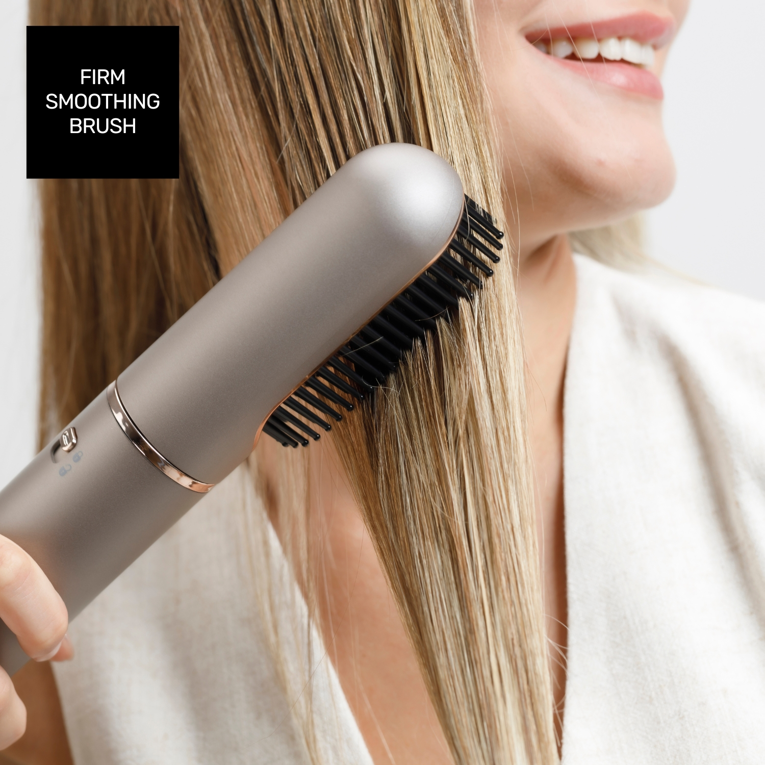 Una mujer usa un cepillo alisador en su cabello rubio. El cepillo es plateado y negro. Ella está sonriendo.