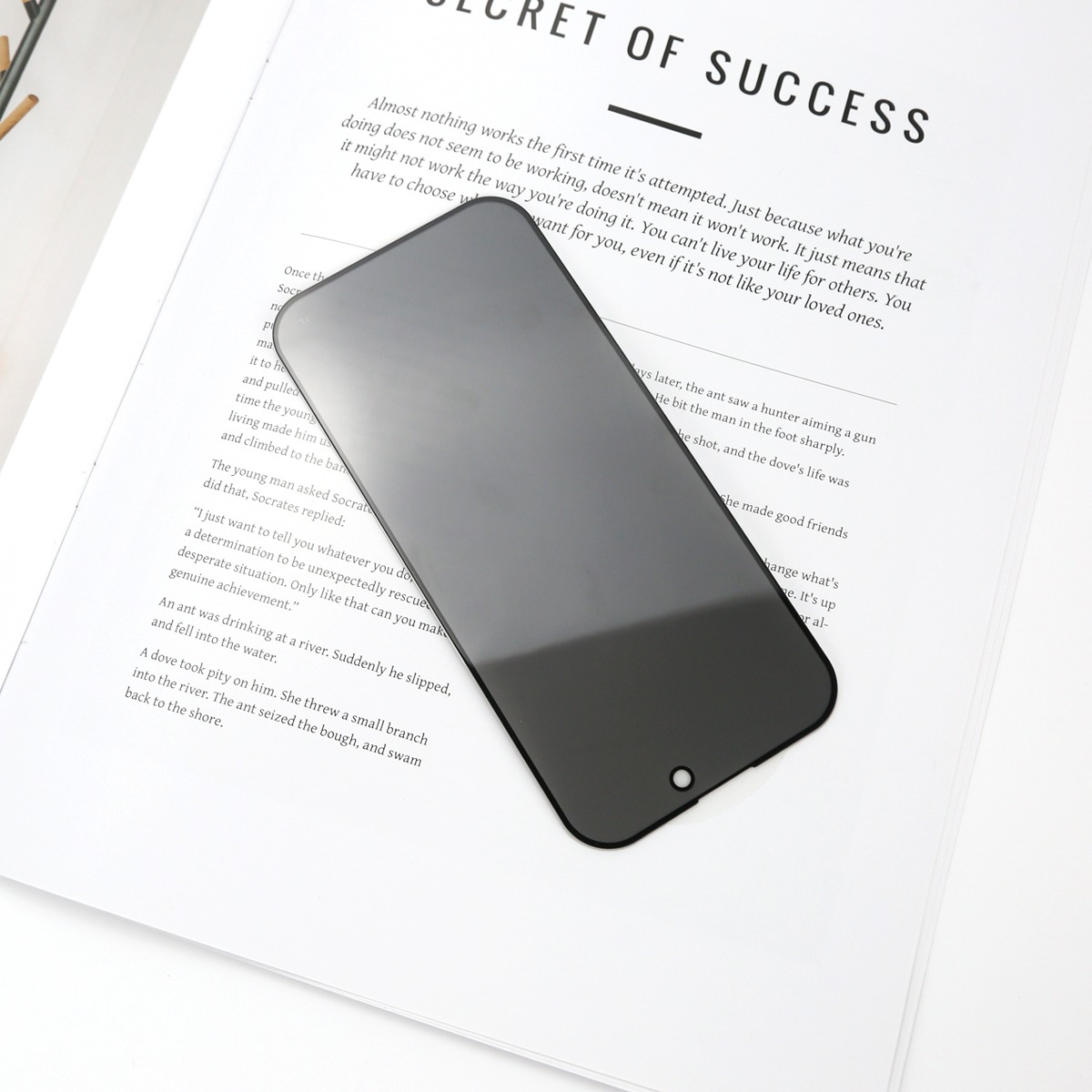 Schwarzer Telefonbildschirm auf weißem Papier mit dem Text 'SECRET OF SUCCESS'. Das Telefon befindet sich im Vordergrund.