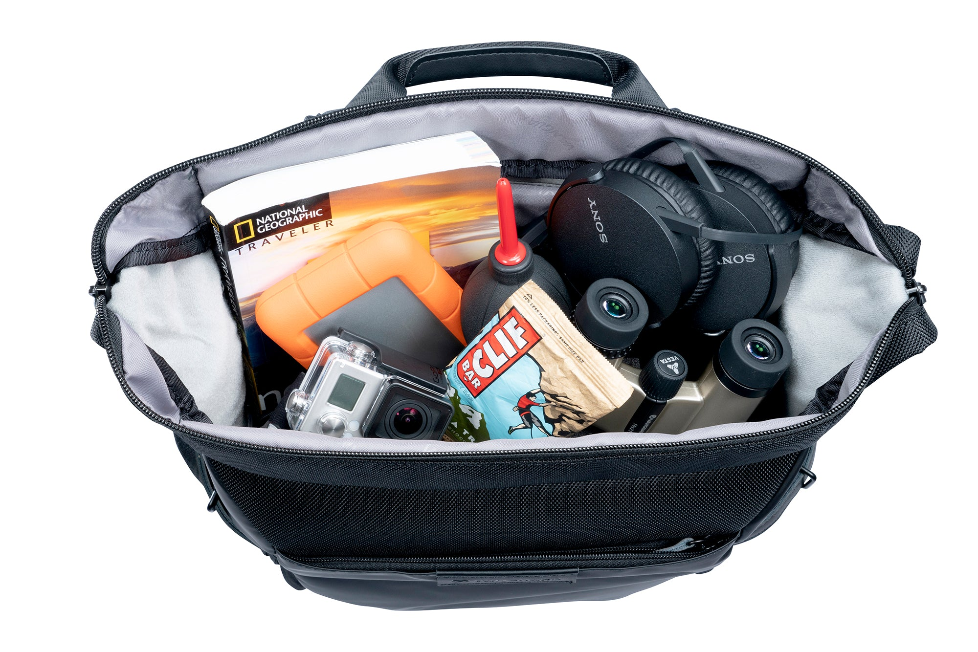 Eine schwarze Tasche mit Kopfhörern, Kamera, Fernglas, Buch, orangefarbener Festplatte, Snacks und einem Kamera-Reinigungswerkzeug.