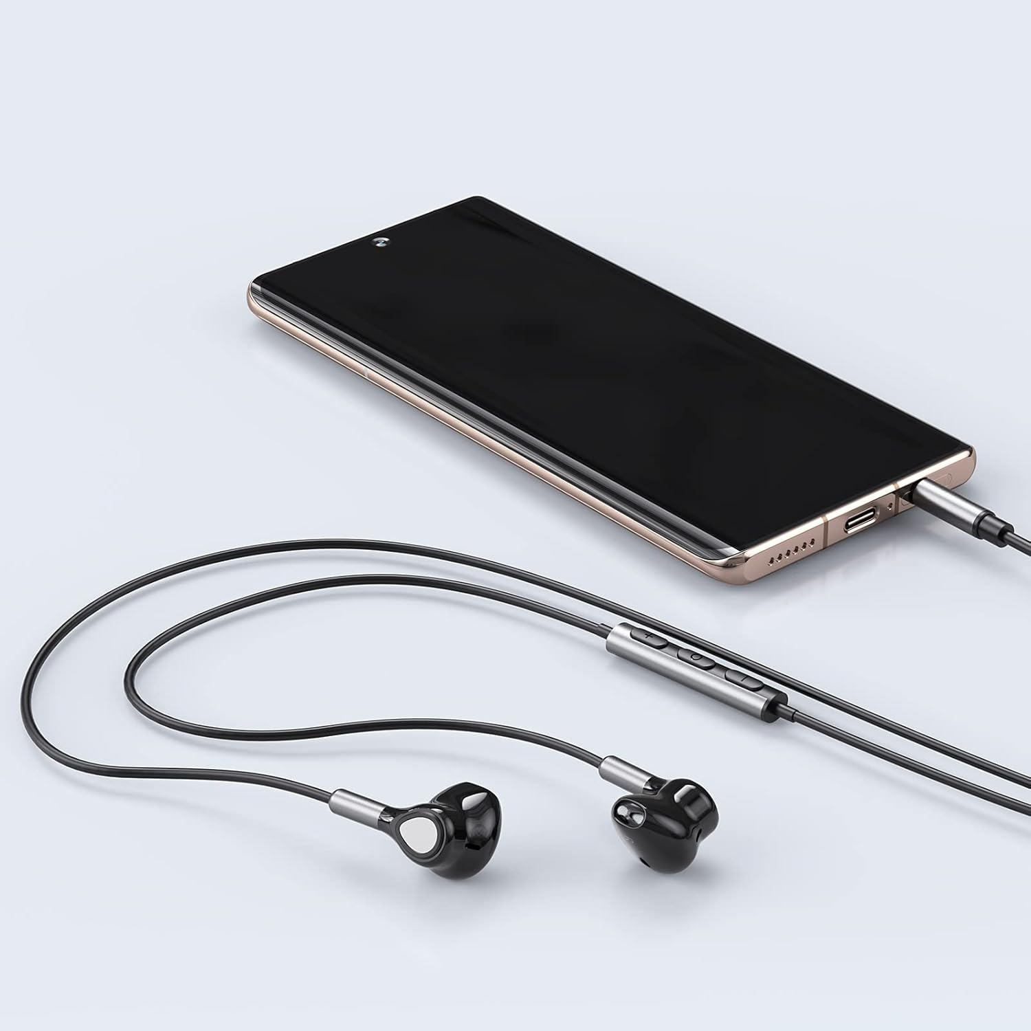 Ein schwarzes Smartphone mit goldfarbenem Rand ist mit schwarzen Kopfhörern verbunden. Die Kopfhörer und das Telefon liegen auf einer weißen Oberfläche.