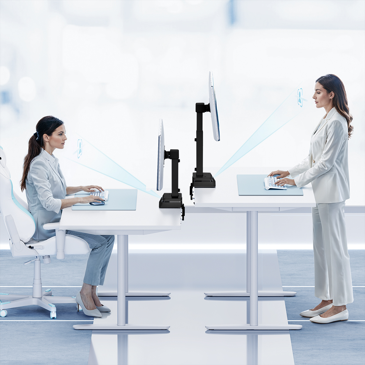 Due donne alle scrivanie, una seduta, una in piedi, usano tastiere con monitor. La scena è luminosa e moderna.