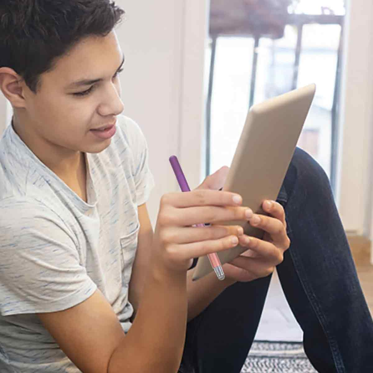 Ein junger Mann hält ein Tablet und einen Stift und schaut auf das Tablet. Er trägt ein helles T-Shirt und Jeans. Der Hintergrund ist unscharf.