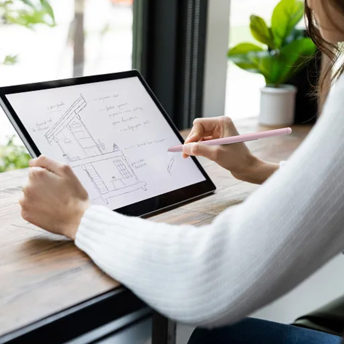 Eine Person skizziert mit einem rosa Stift auf einem Tablet. Die Zeichnung zeigt einen Hausplan. Im Hintergrund eine Pflanze in einem weißen Topf.
