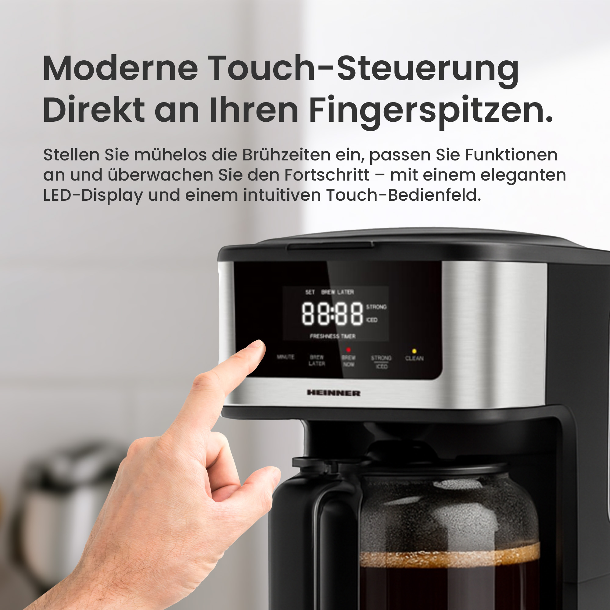 Eine Hand berührt den Bildschirm einer Kaffeemaschine. Der Bildschirm zeigt die Zeit an. Die Maschine hat eine Glaskaraffe.